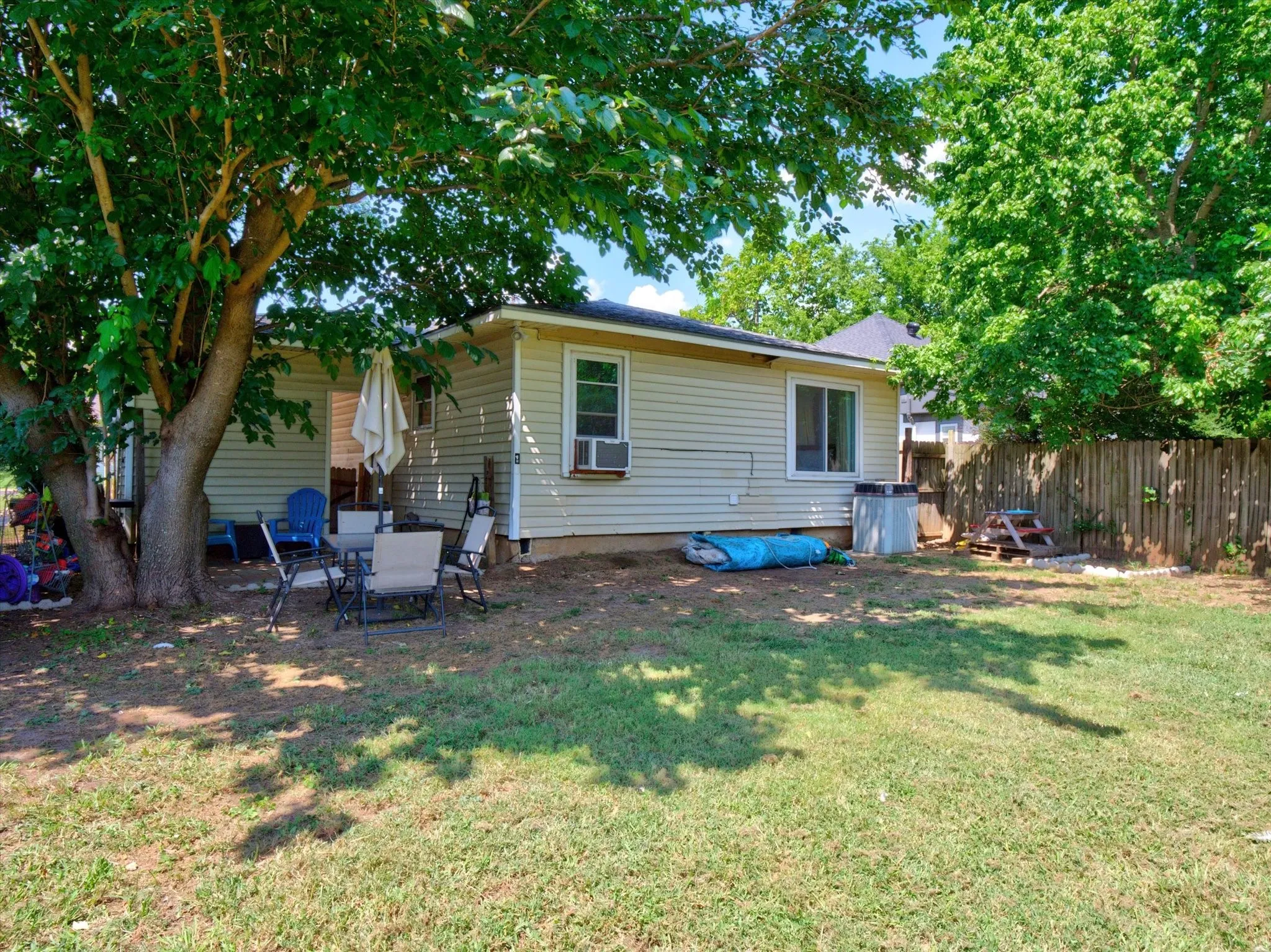 Expansive backyard featuring a mature shade tree, a section of wood privacy fencing, and a rear exterior wall with horizontal siding