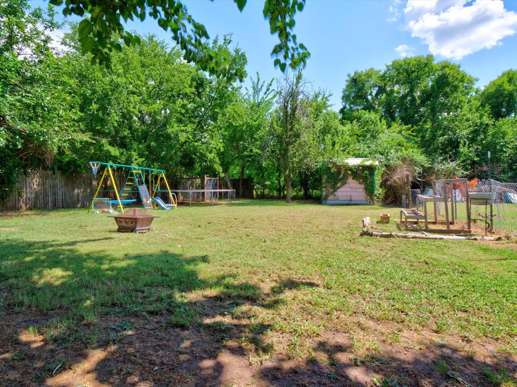 Expansive backyard featuring a large grassy area, mature perimeter trees, and a wooden privacy fence