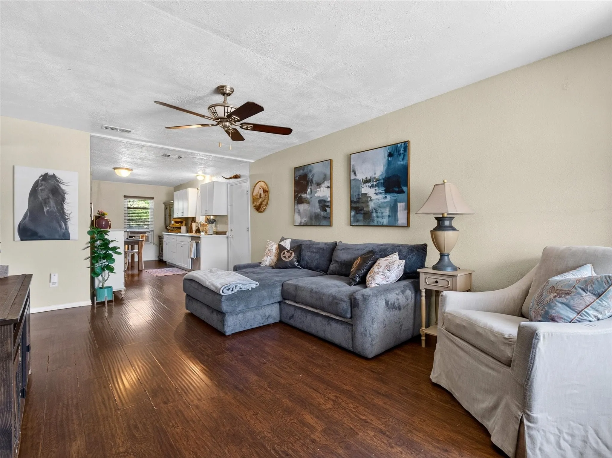 Spacious living area featuring rich wood-finish flooring, a ceiling fan with integrated lighting, and neutral wall tones