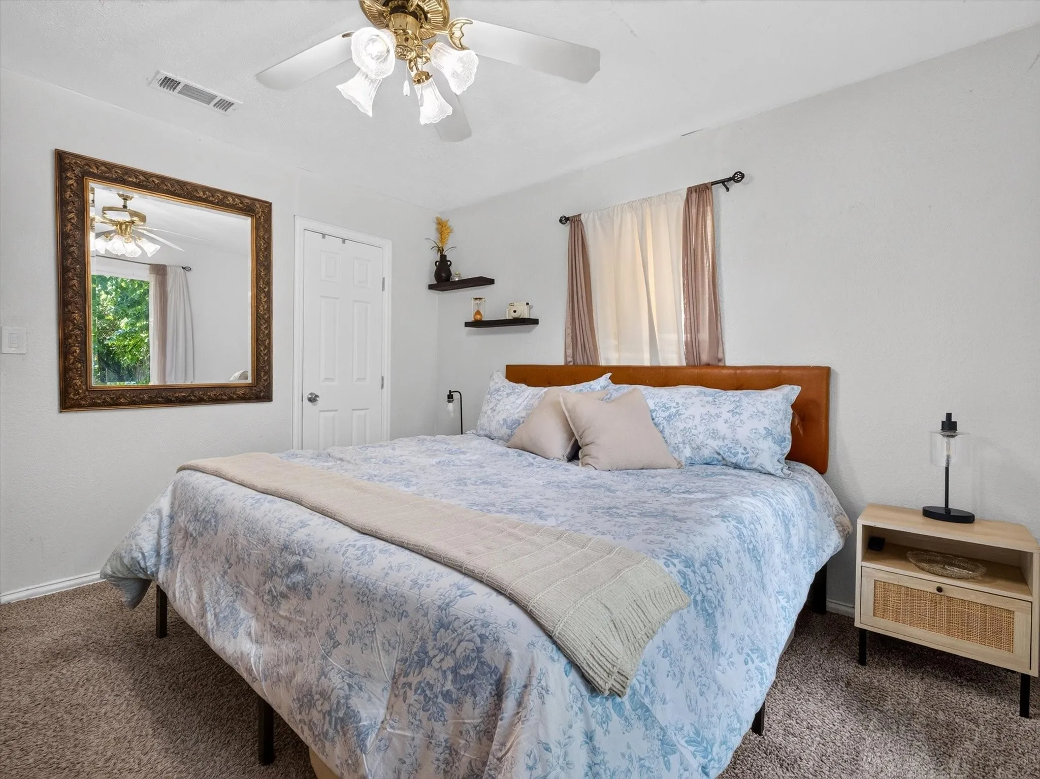 Carpeted bedroom featuring a ceiling fan with light fixture, a window with curtains, and a solid door