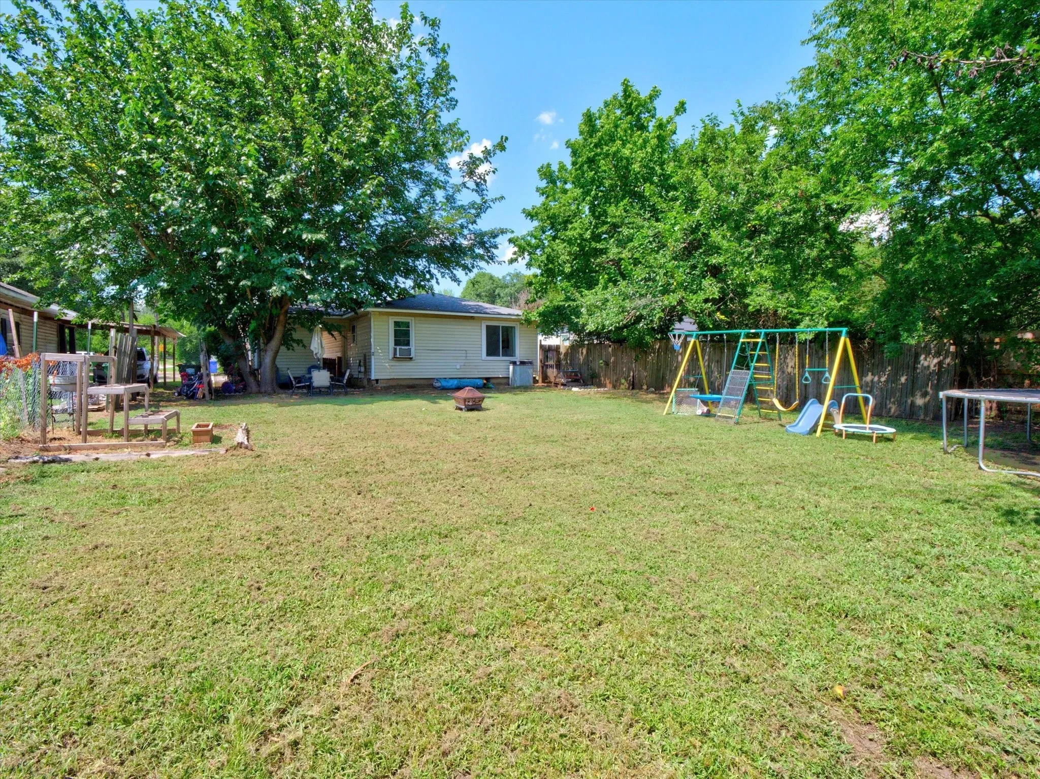 Spacious backyard featuring a large tree providing shade, a wood privacy fence, and a visible portion of the property's exterior