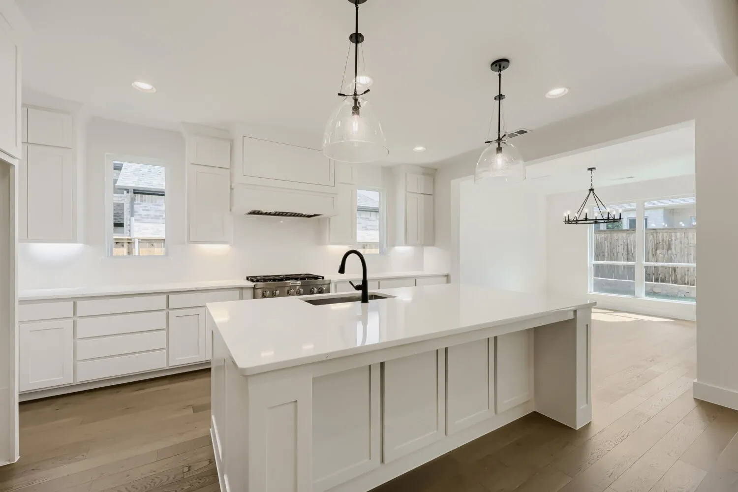 Kitchen featuring white cabinetry, light-toned countertops, a center island with pendant lighting, a stainless steel range, and wood-finish flooring