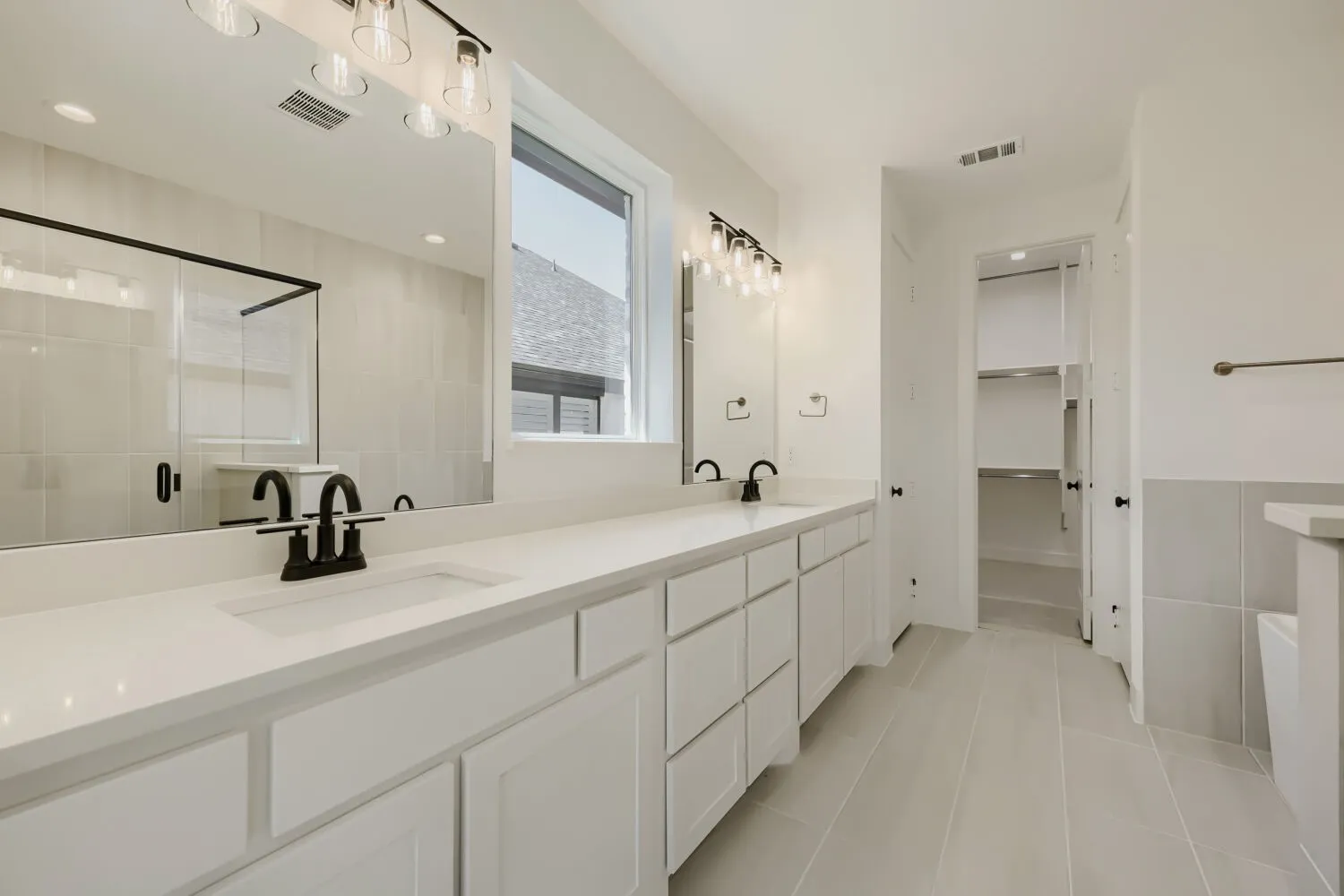 Spacious bathroom featuring a dual vanity with white cabinetry, light-toned countertops, and matte black fixtures