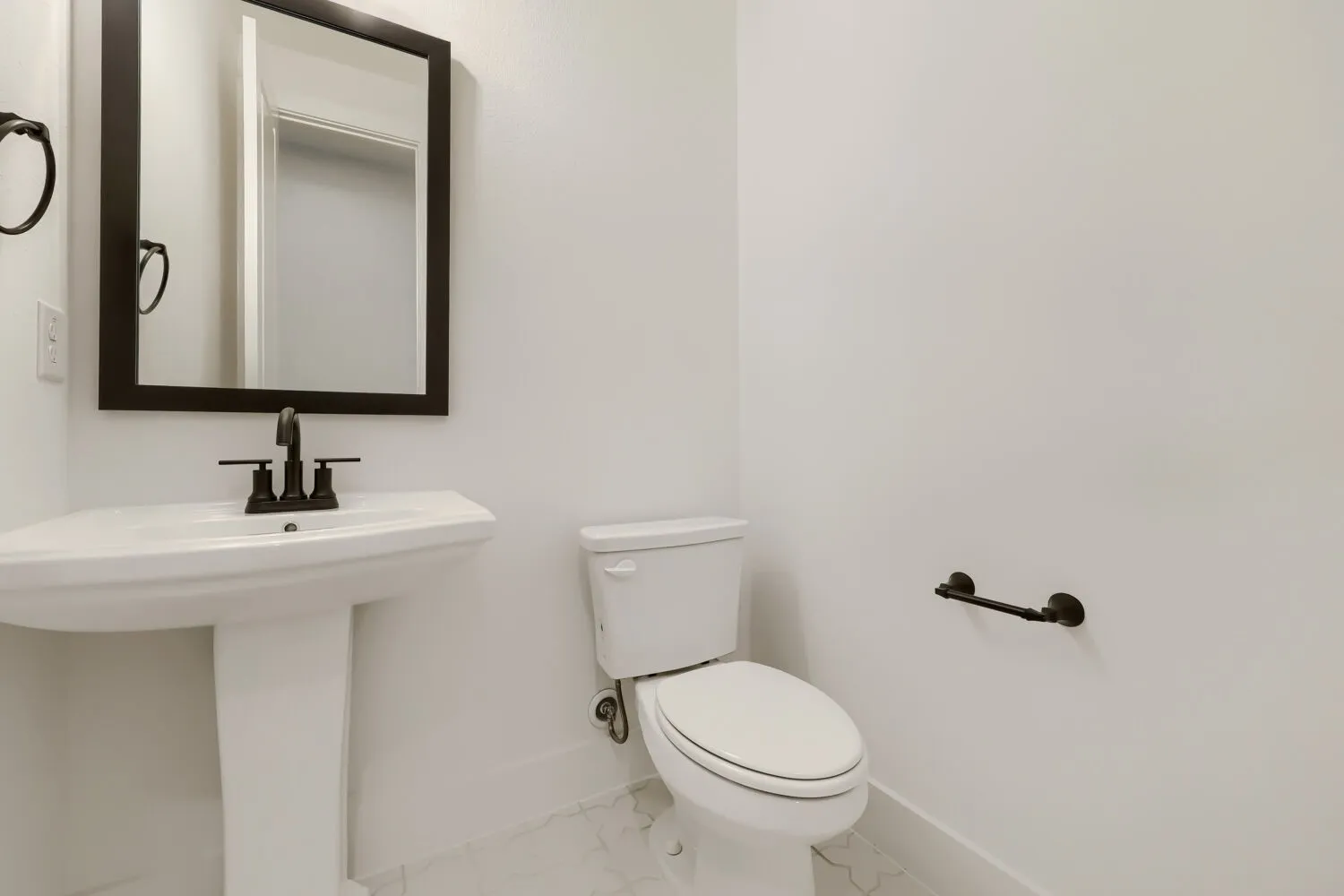 Contemporary powder room featuring a white pedestal sink, oil-rubbed bronze fixtures, a matching framed mirror, and hexagonal tile flooring
