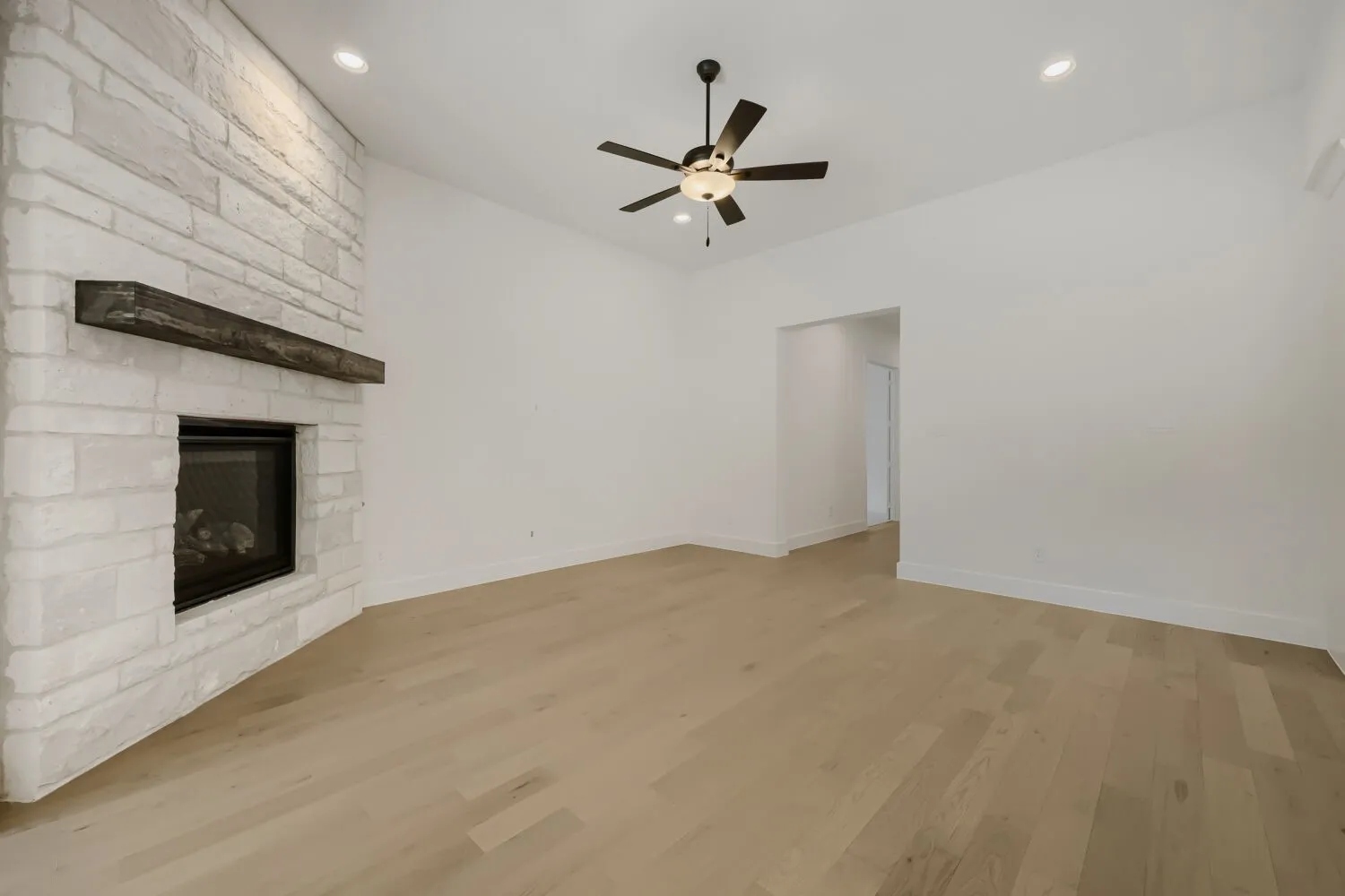Living area featuring a floor-to-ceiling stone fireplace with a wood mantel, wood-finish flooring, recessed lighting, a ceiling fan with integrated lighting, and an open entryway to an additional room