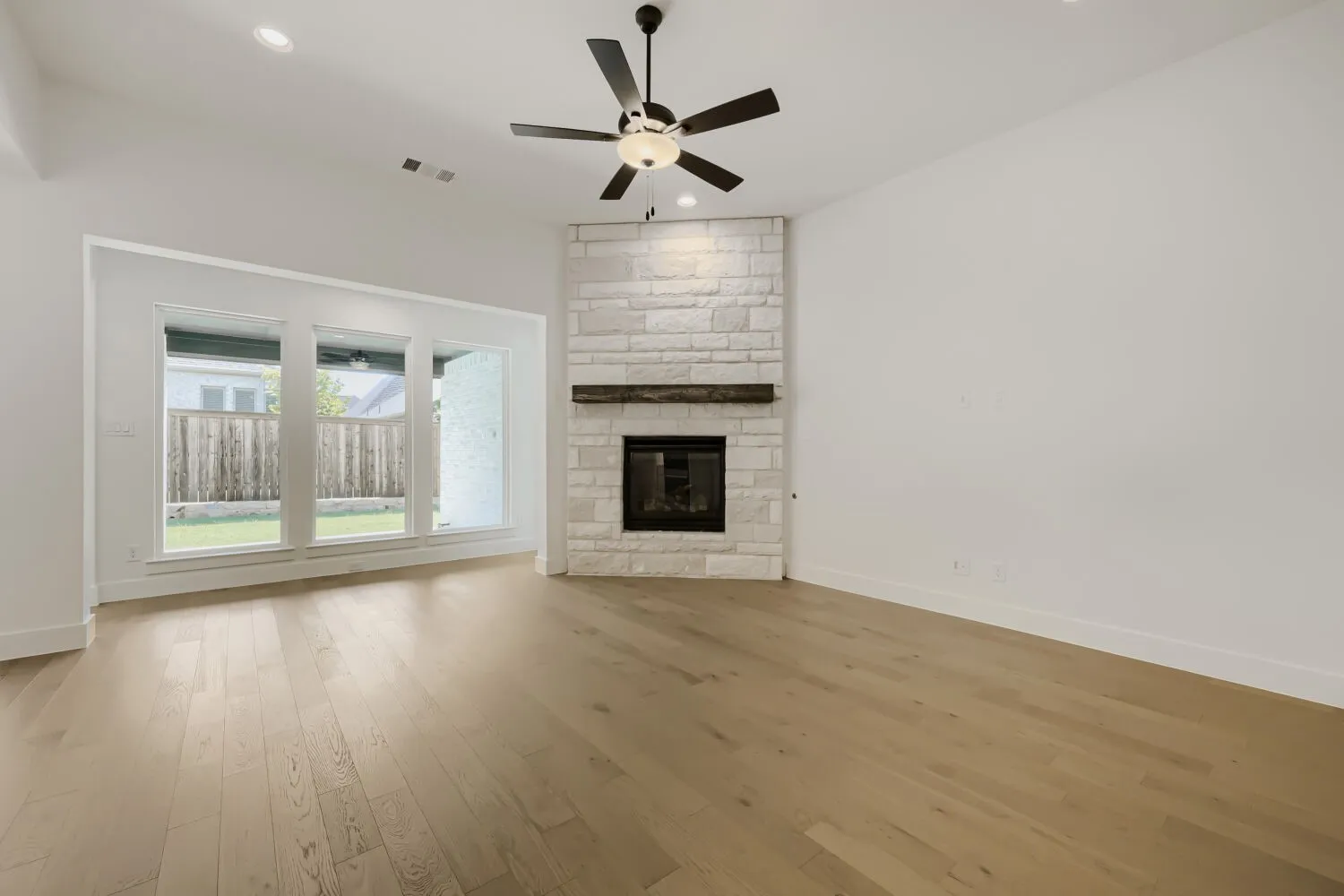 Spacious interior with high vaulted ceilings, light wood-finish flooring, and a stone-clad fireplace featuring a wood mantel