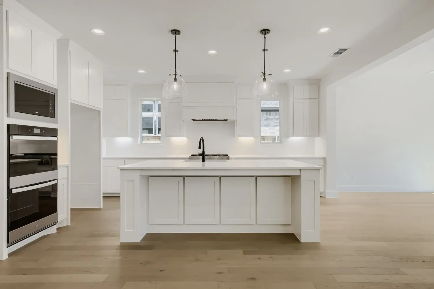 Expansive kitchen featuring a large central island, integrated stainless steel appliances, abundant white cabinetry, and wood-finish flooring