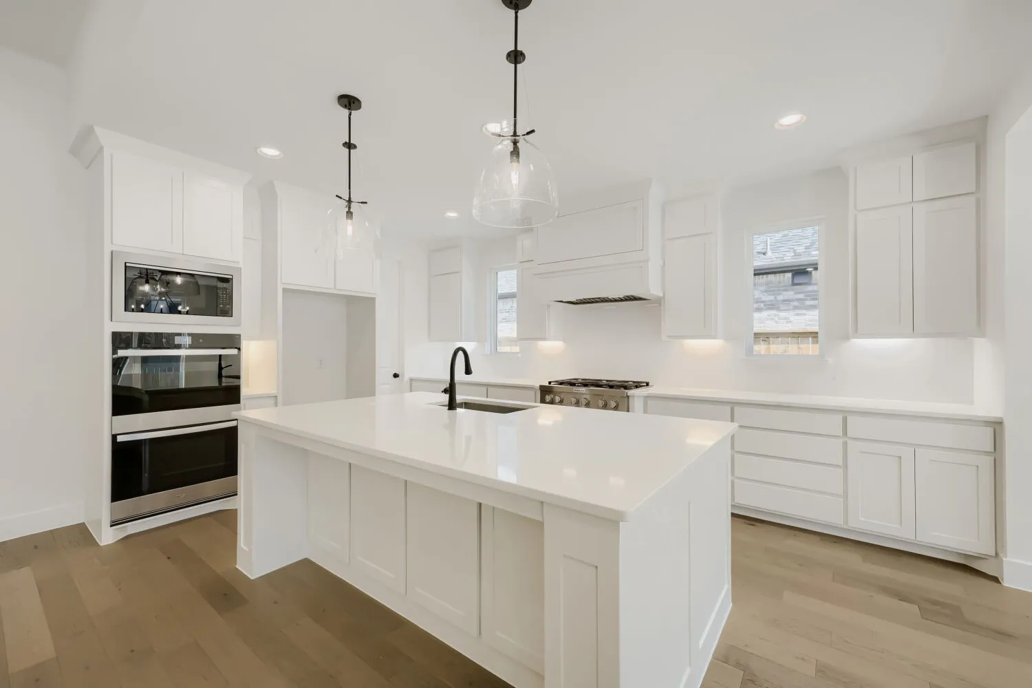 Bright kitchen featuring an expansive center island with a white countertop, extensive white cabinetry, built-in stainless steel appliances, and wood-finish flooring