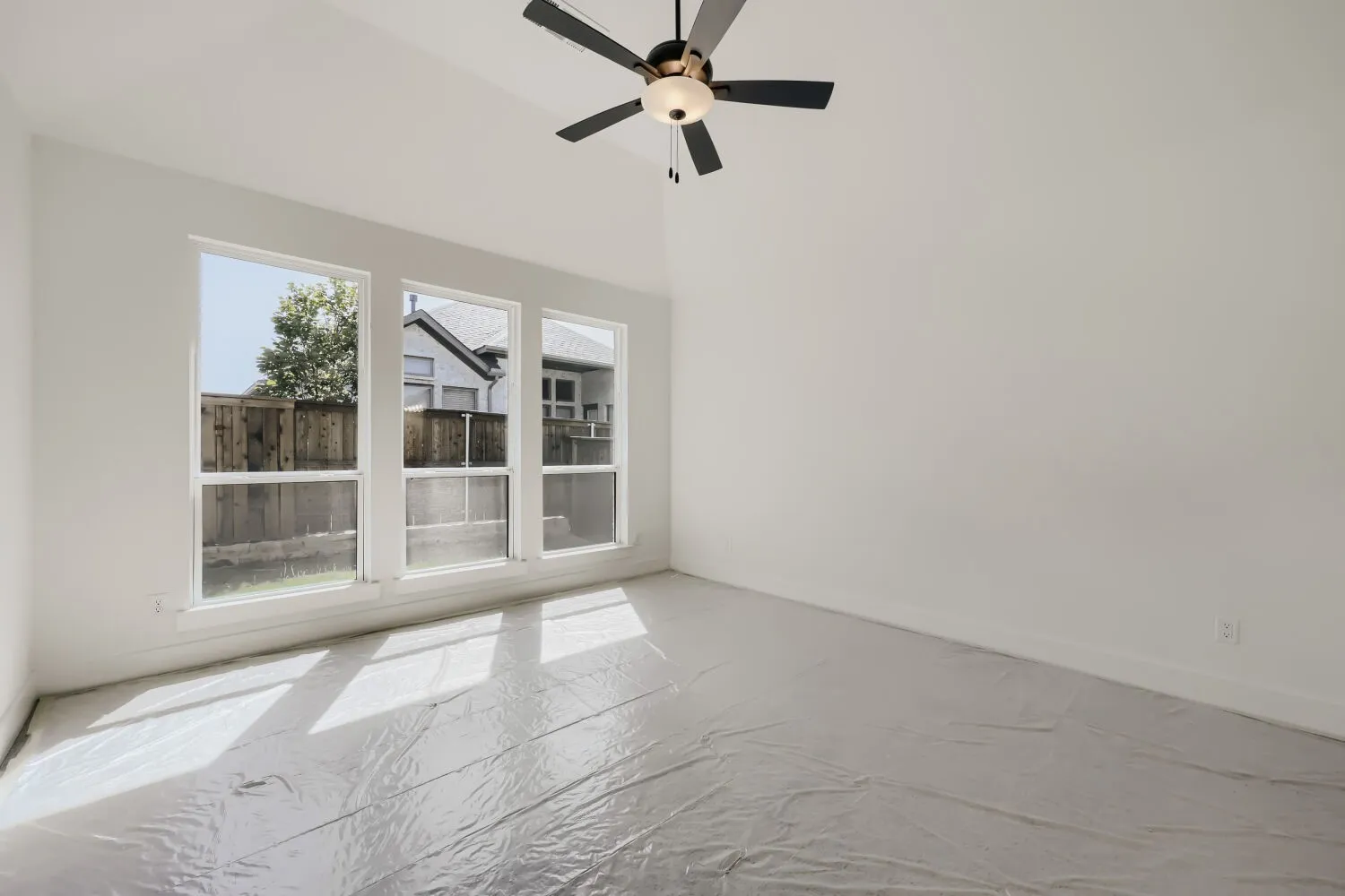 Vaulted ceiling room featuring three large windows, a contemporary ceiling fan with light fixture, white painted walls, and white baseboards