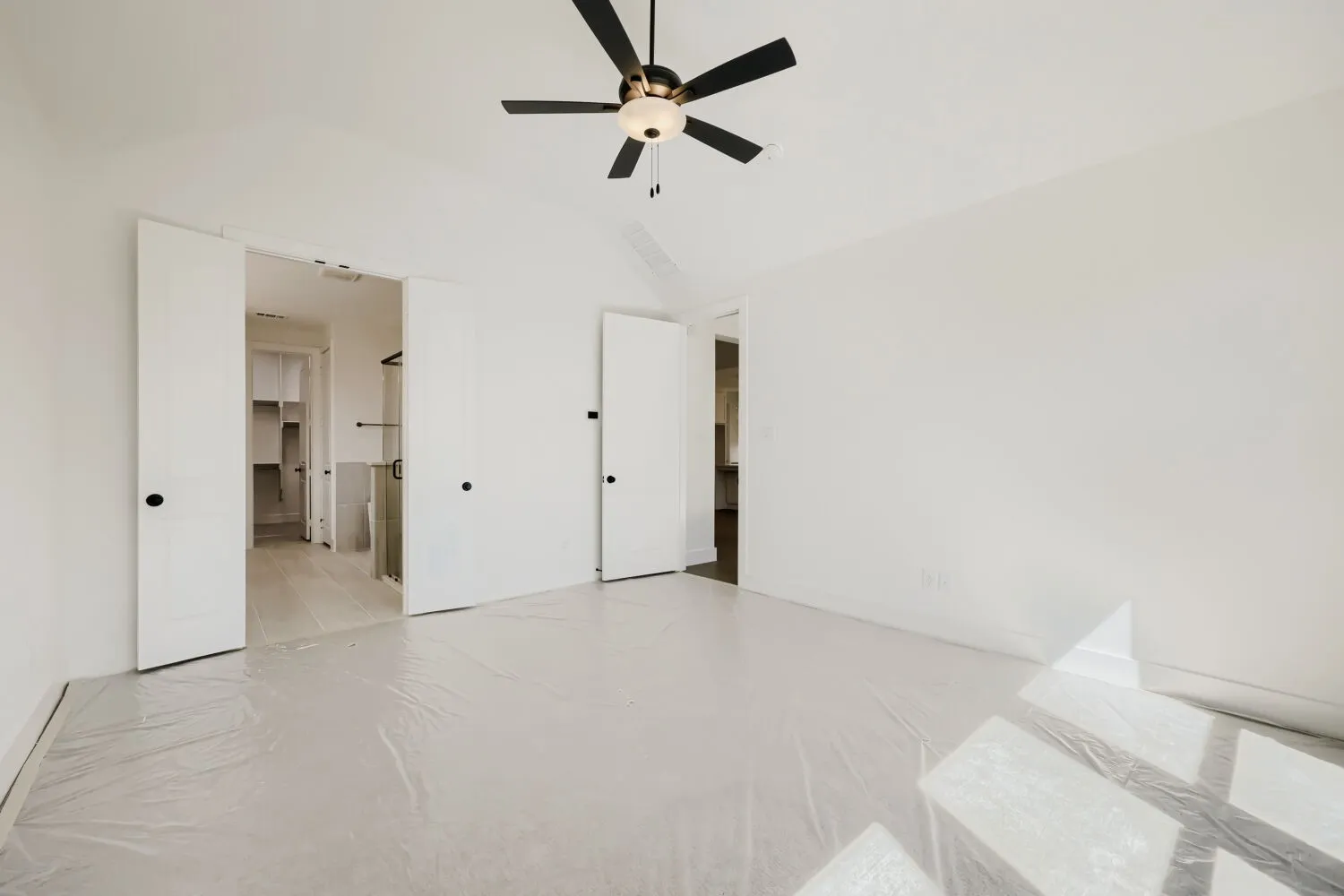 Spacious room with a ceiling fan, white walls, and a door opening to a walk-in closet with built-in shelving