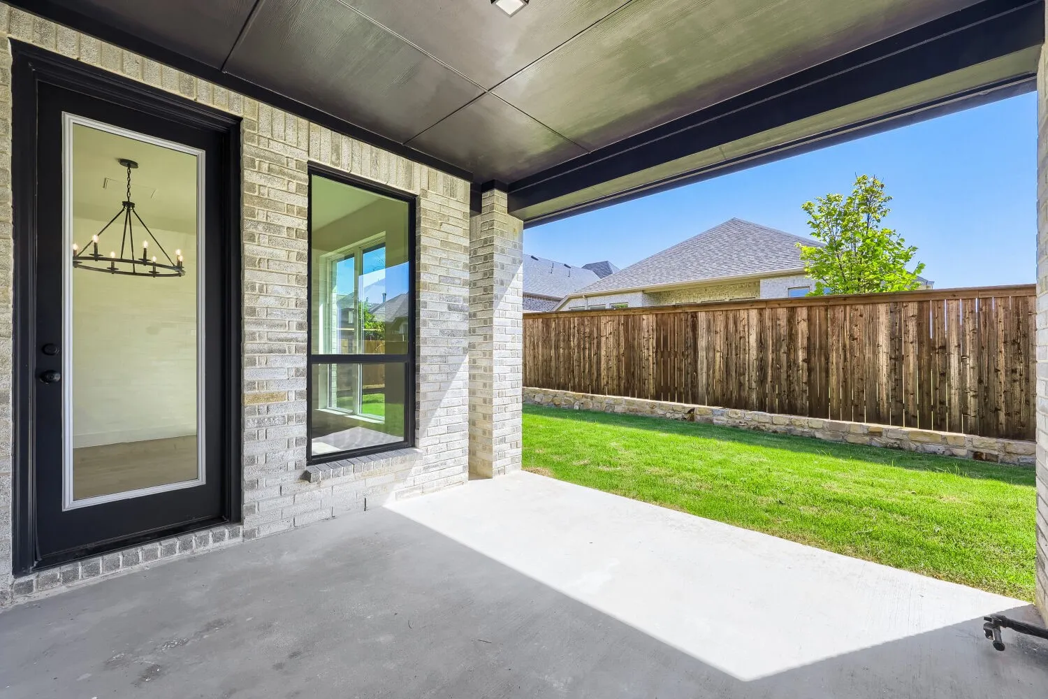Covered concrete patio with a light brick exterior and an expansive green lawn