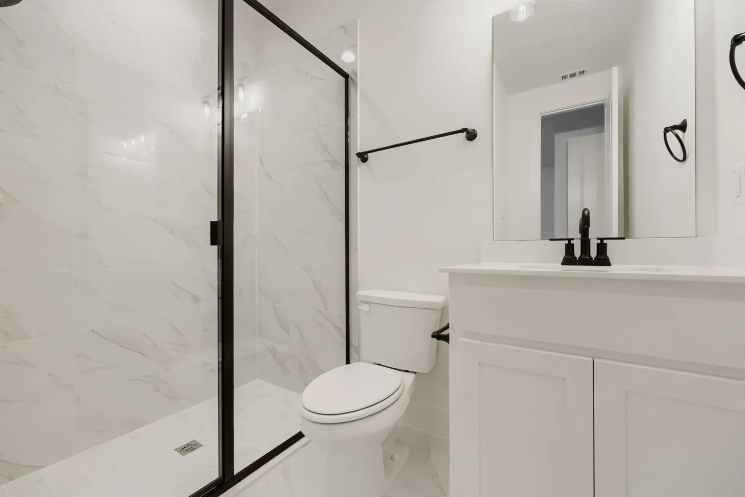 Modern bathroom featuring a walk-in shower with black-framed glass enclosure, marble-look tile, and a single vanity with storage cabinetry, white countertop, and black fixtures