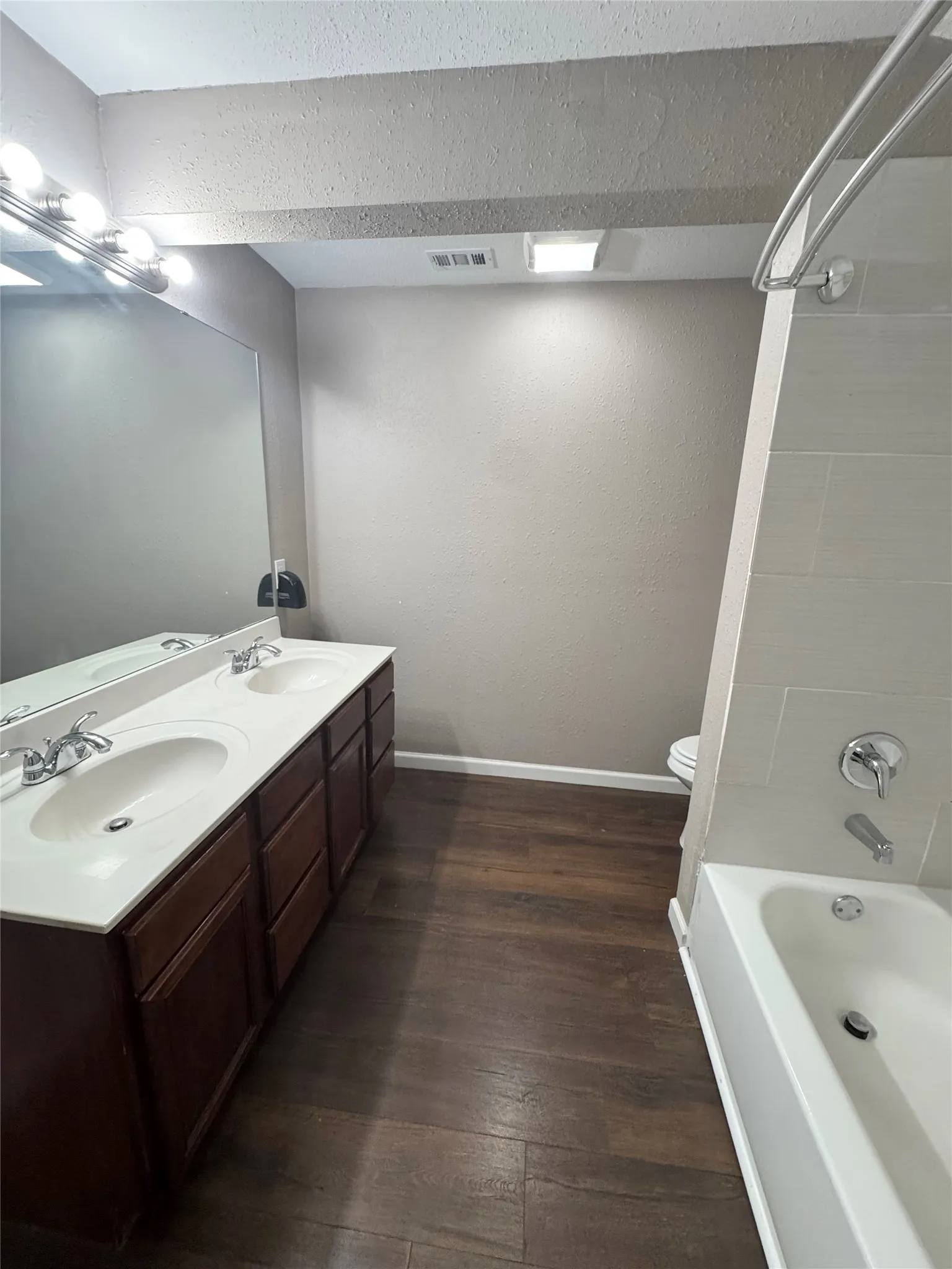 Bathroom featuring a double vanity with wood cabinetry and an integrated countertop, wood-finish flooring, and a white bathtub with subway tile surround
