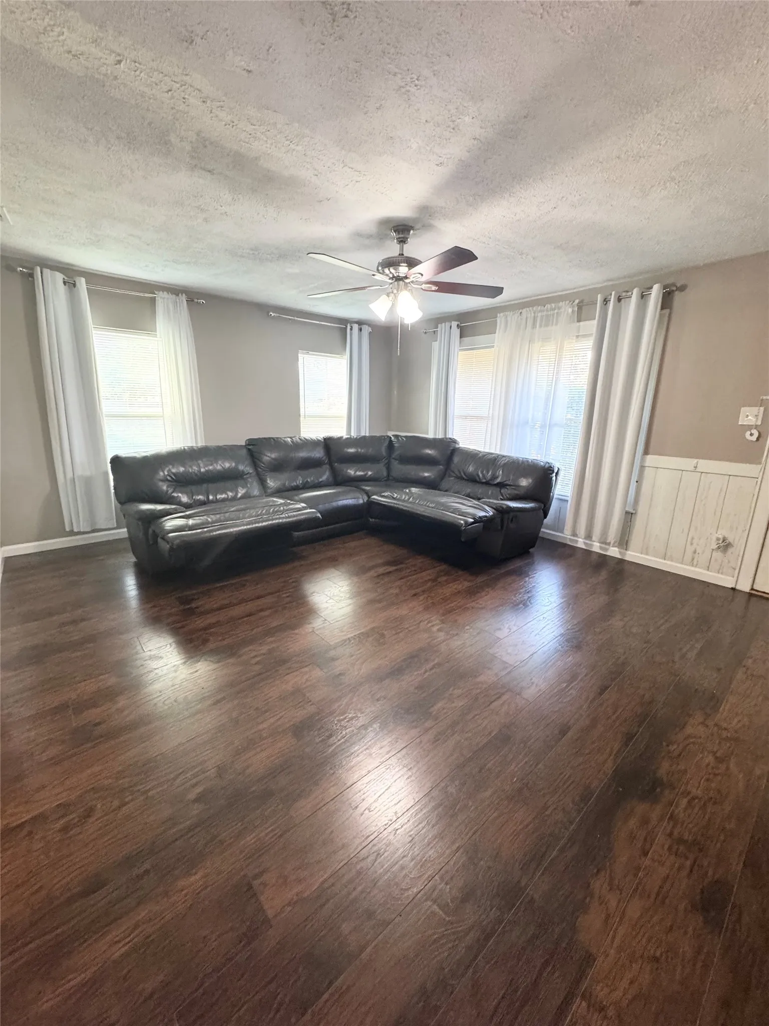 Spacious interior featuring wood-finish flooring, a ceiling fan with integrated lighting, and multiple windows