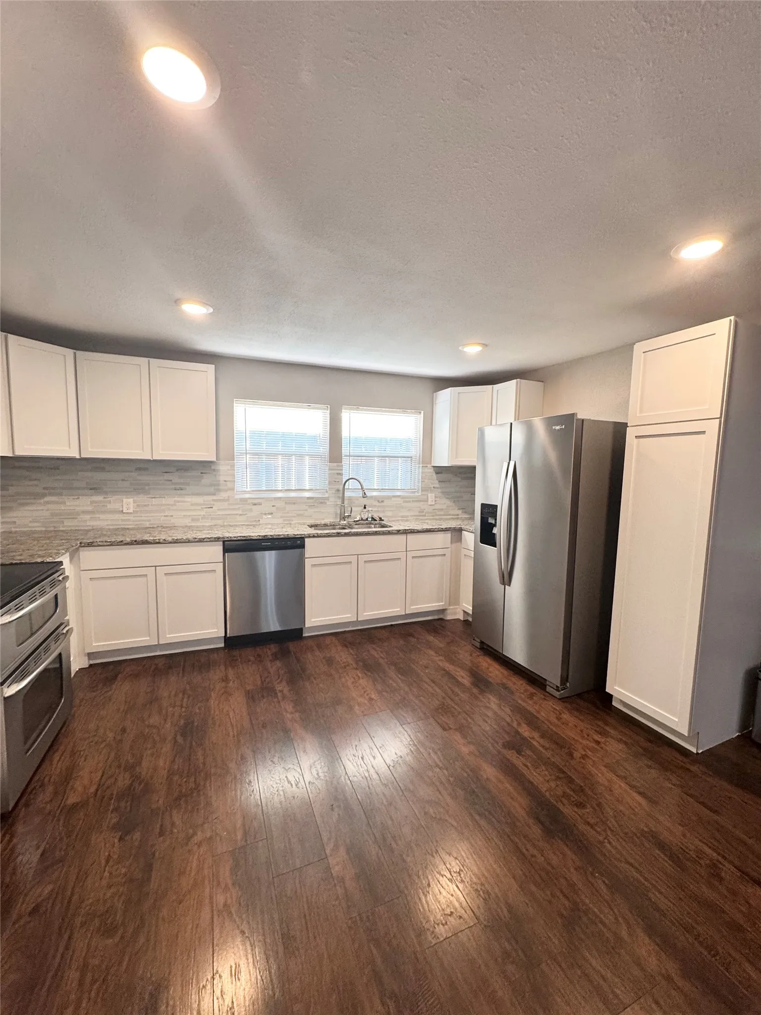 Kitchen featuring stainless steel appliances, white cabinetry, granite countertops, a tiled backsplash, and wood-finish flooring