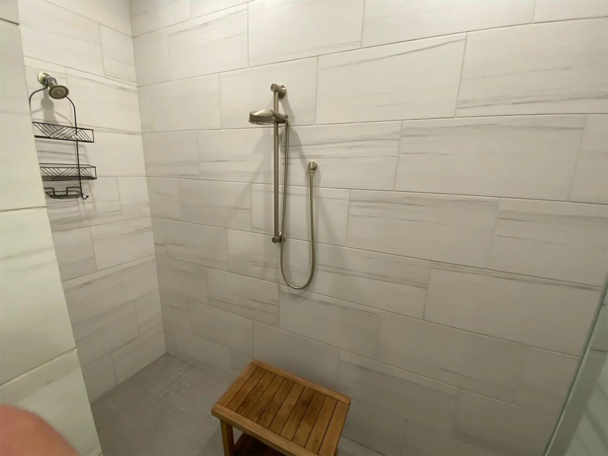 Walk-in shower featuring large format white tile walls, a handheld shower fixture, and a built-in shower head