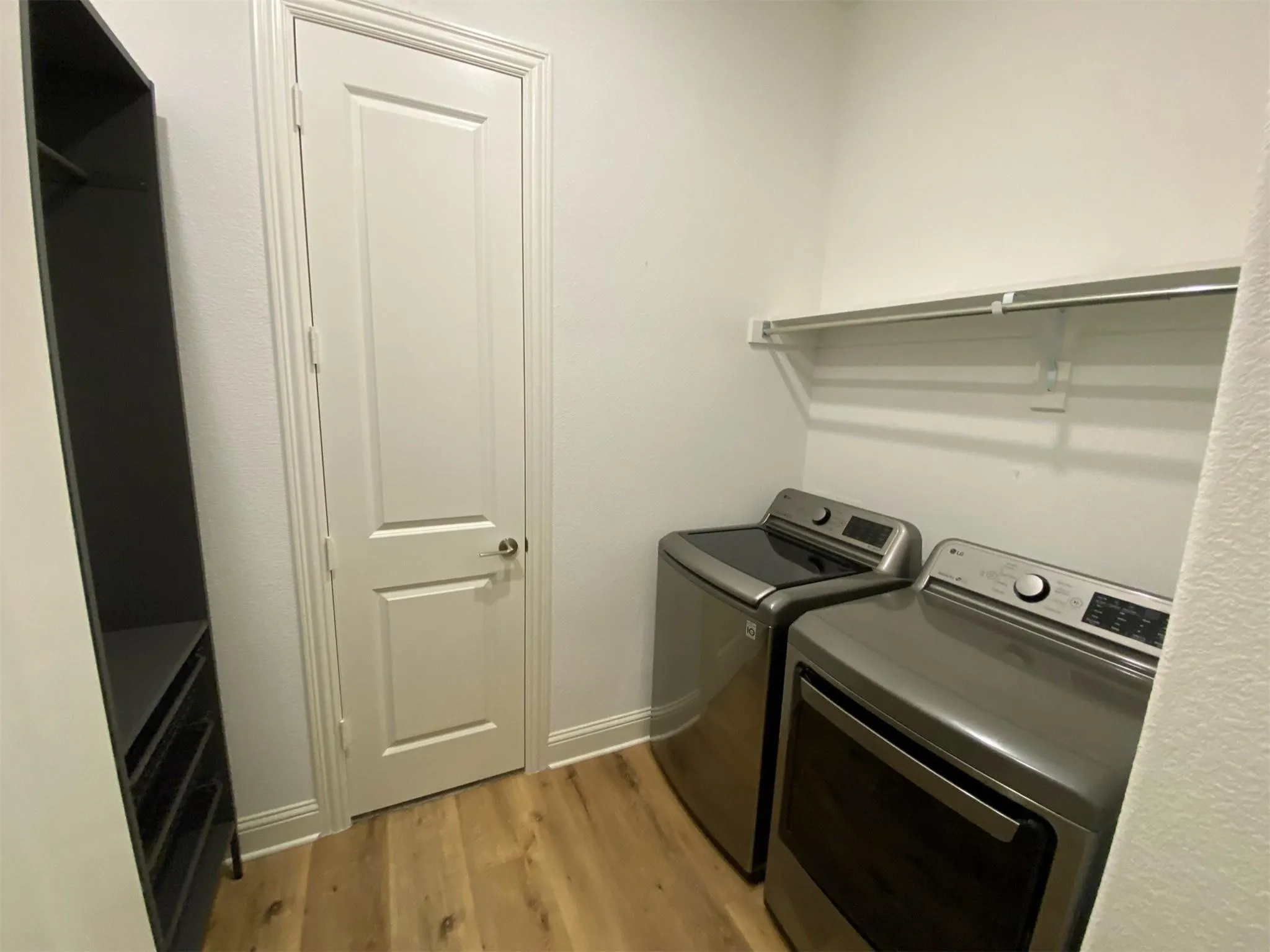 Dedicated laundry area featuring wood-finish flooring and a white built-in shelf with hanging rod