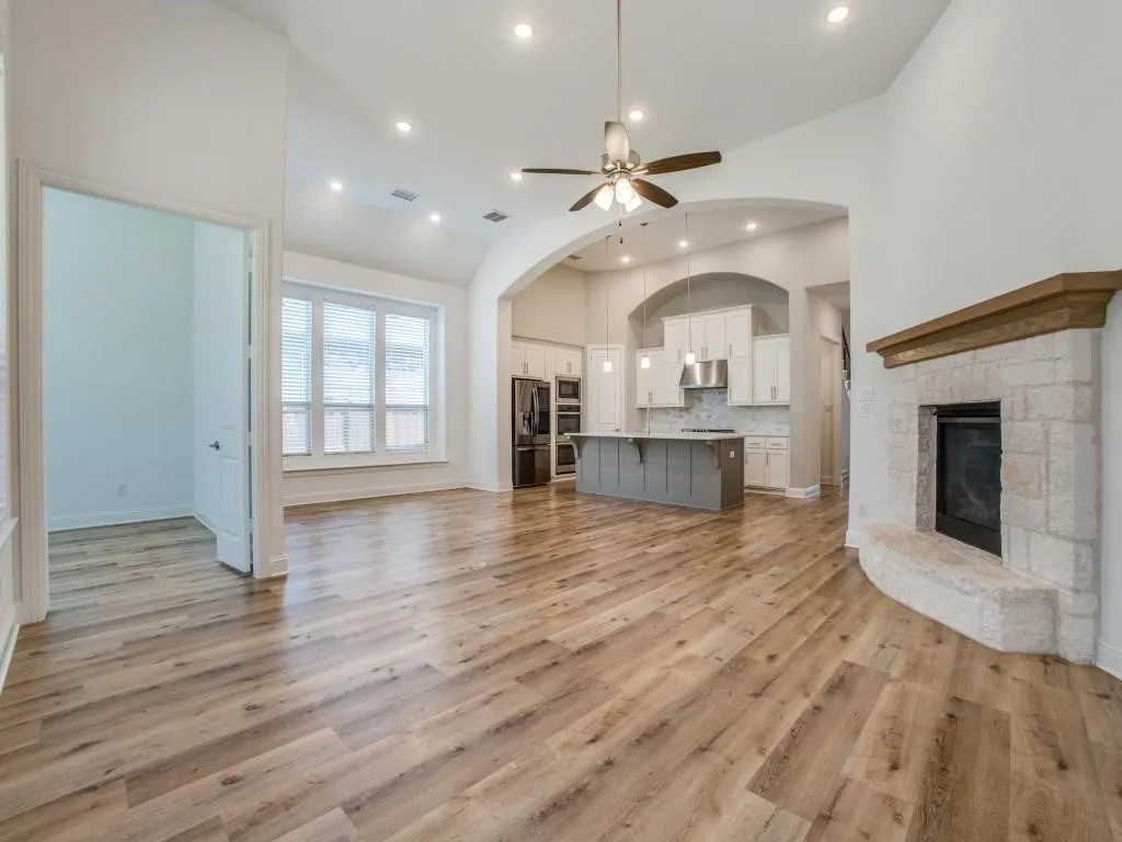 Spacious living area featuring wood-finish flooring, a stone-clad fireplace with a wood mantle, and multiple recessed lighting fixtures