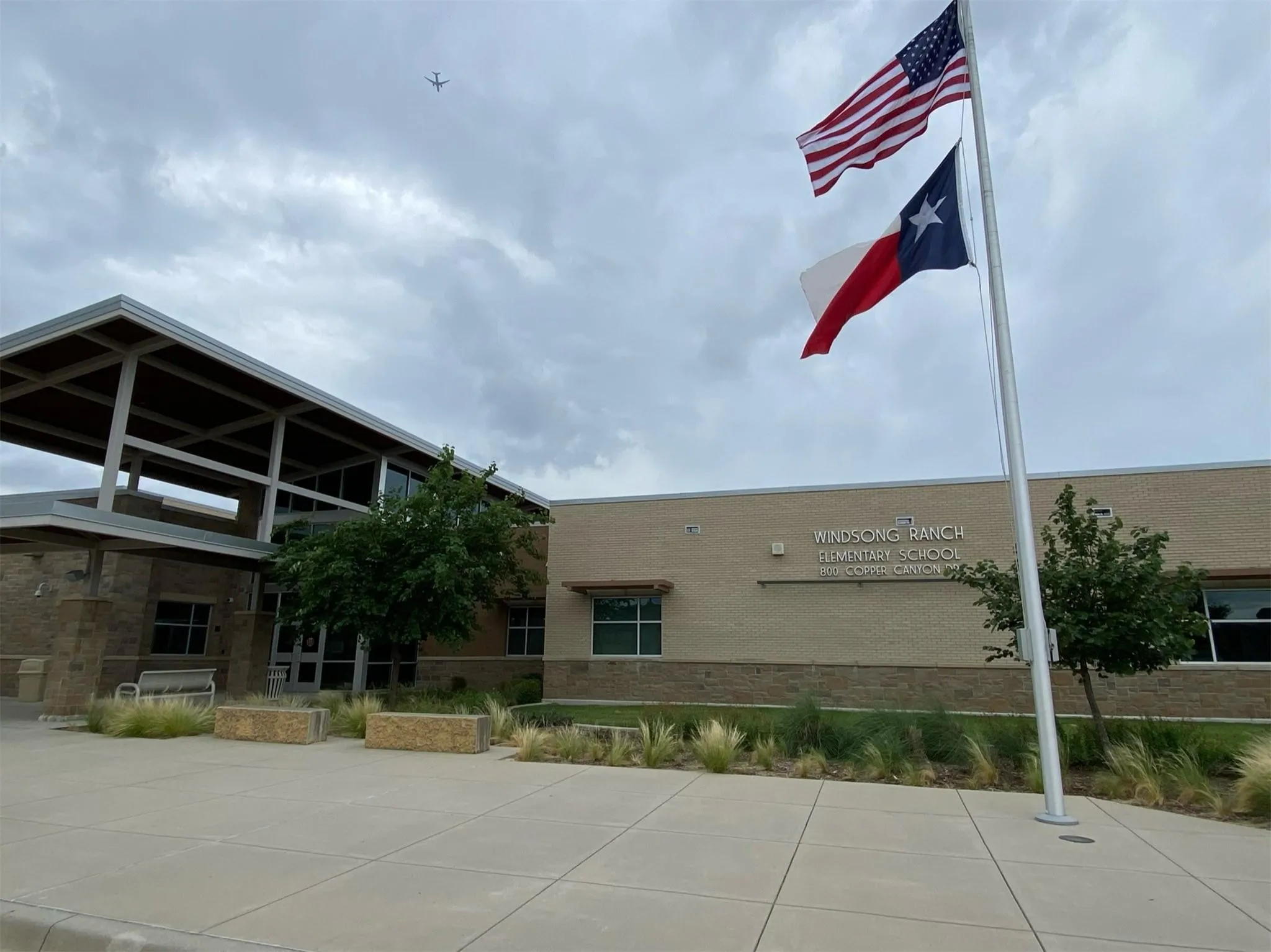 Flagpole with American and Texas flags in front of a brick and stone building, featuring a covered entry and landscaping