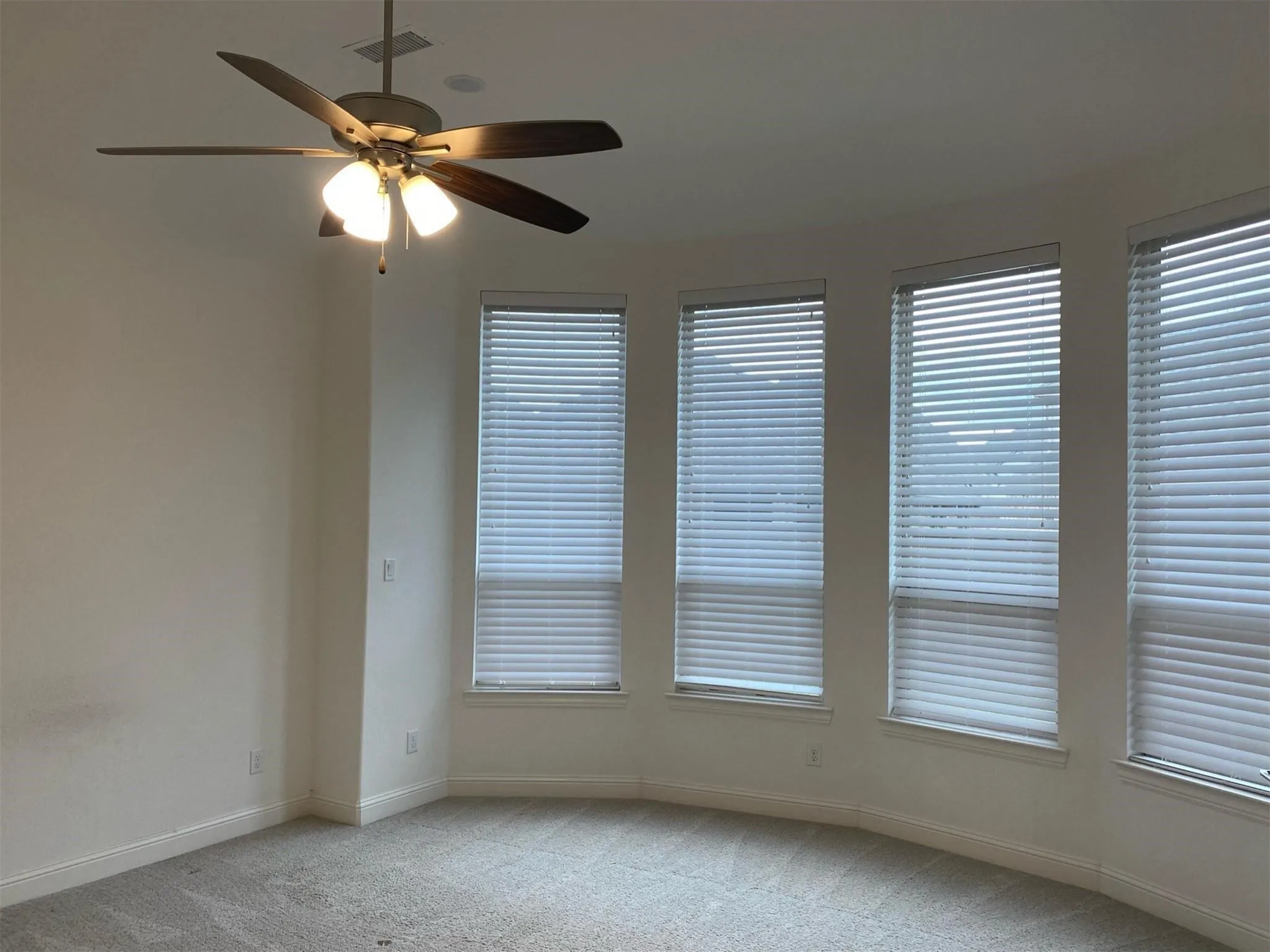 Room featuring a curved bay window with multiple windows, a ceiling fan with integrated lighting, and neutral-toned carpet flooring