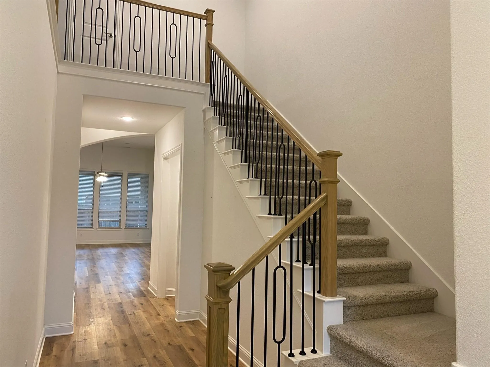 Staircase featuring carpeted treads, white risers, and a wood-finish handrail with black iron balusters