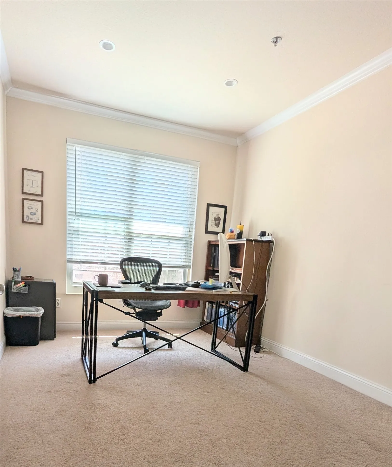 Recessed lighting and crown molding accentuate this space featuring a large window with blinds, light-toned carpeting, and white baseboards