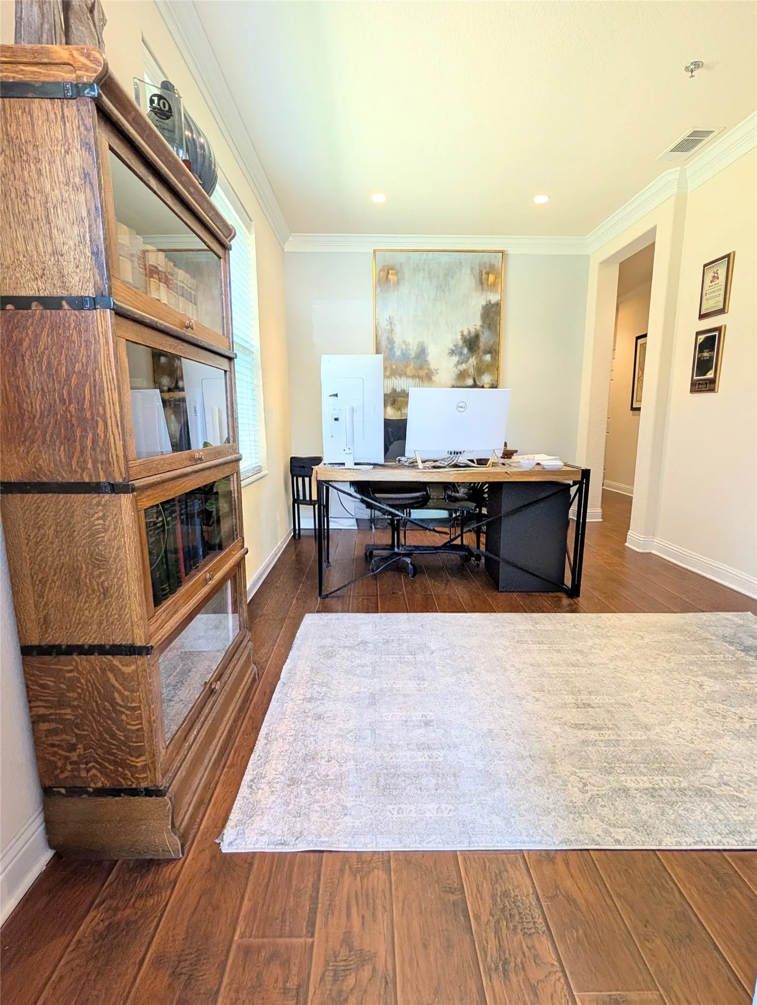 Hardwood-finish flooring throughout this versatile room, featuring crown molding, recessed lighting, and ample natural light from the window