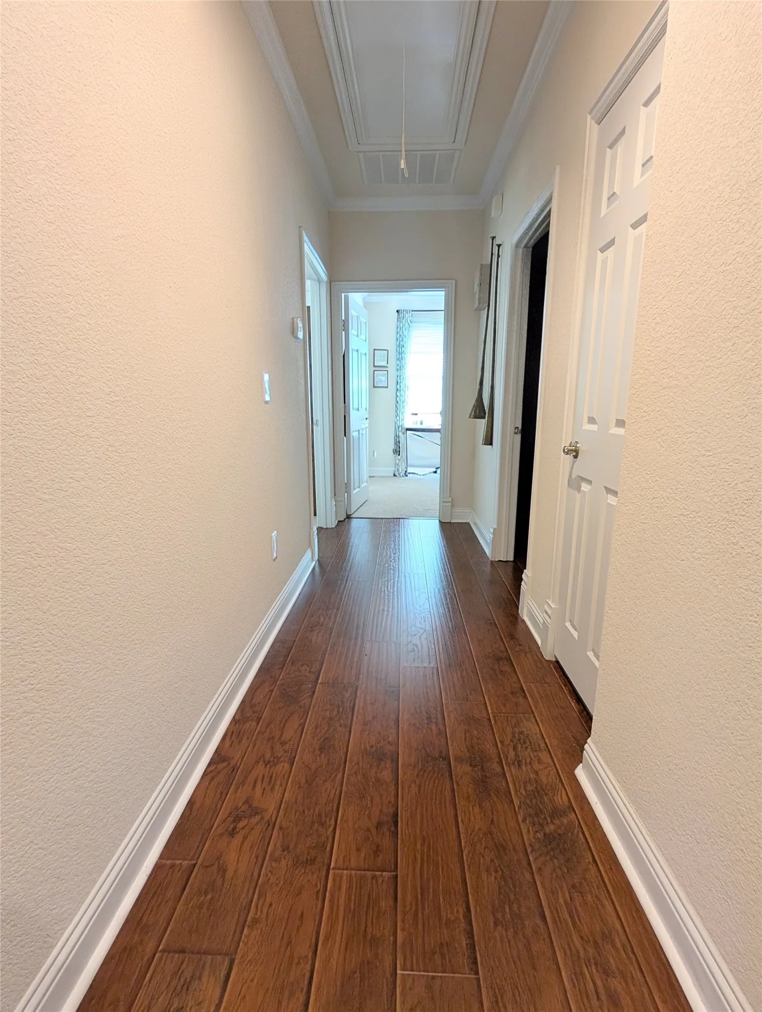 Hallway featuring wood-finish flooring, light-toned walls, white baseboards, and white crown molding