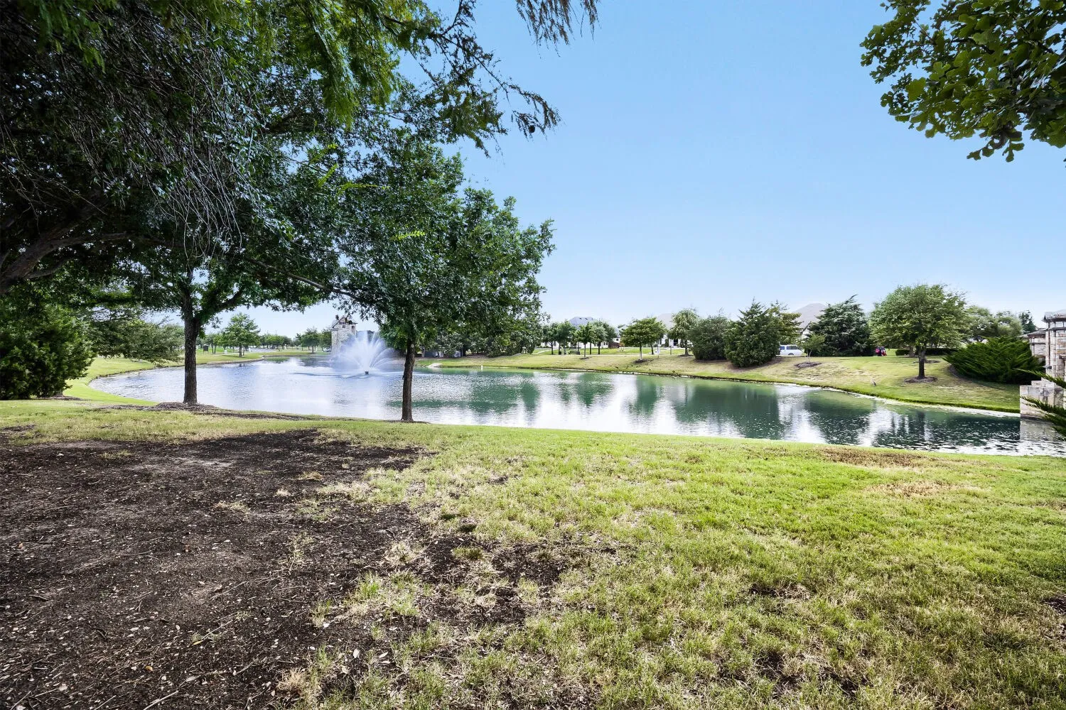 Scenic pond with a central water feature, surrounded by verdant landscaping and mature trees