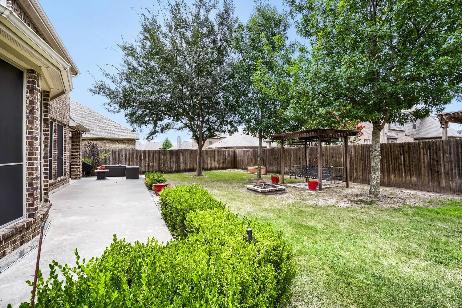 Expansive backyard with a concrete patio, lush green lawn, mature trees, and a privacy fence