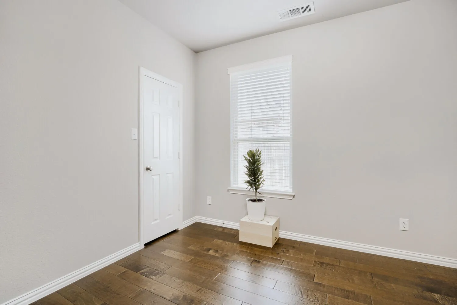 Interior room featuring wood-finish flooring, light gray walls, white baseboards, and a white paneled door
