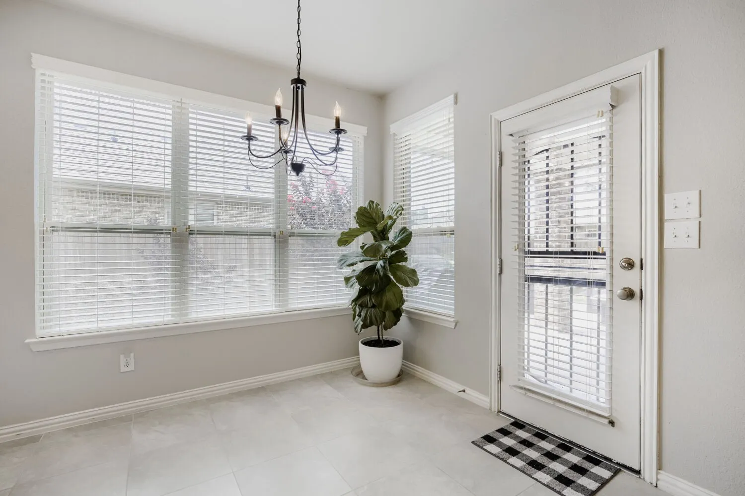 Light gray wall paint complements the light tile flooring in this room featuring a multi-pane window with blinds and a four-light chandelier