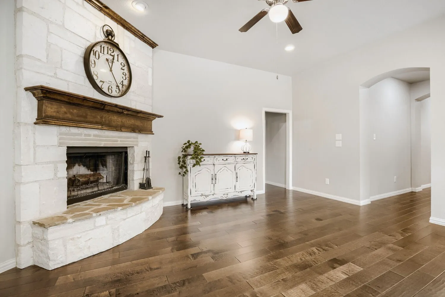 Living area featuring a stone-clad fireplace with a wood mantel, wood-finish flooring, recessed lighting, an arched doorway, and a ceiling fan