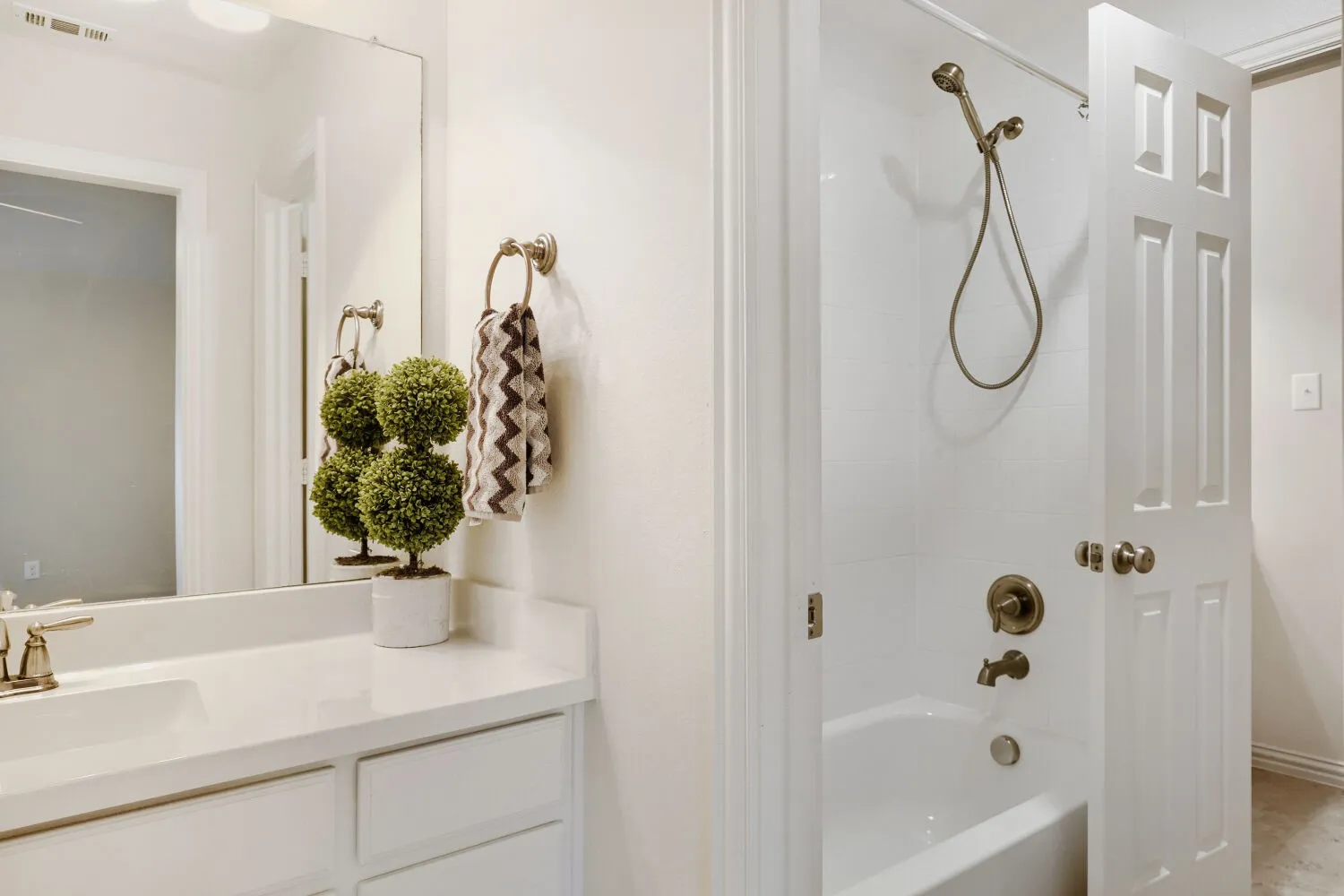 Bathroom featuring a white vanity with an integrated sink, a large wall-mounted mirror, white tile shower surround, a white bathtub, and brushed bronze fixtures