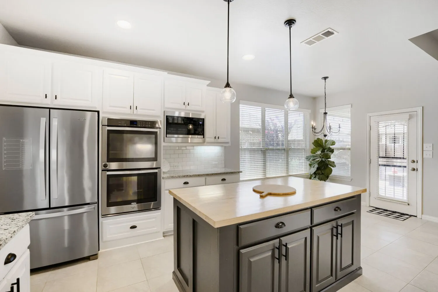 Modern kitchen featuring a central island with a wood-finish countertop, white cabinetry with black hardware, stainless steel appliances, and tile flooring