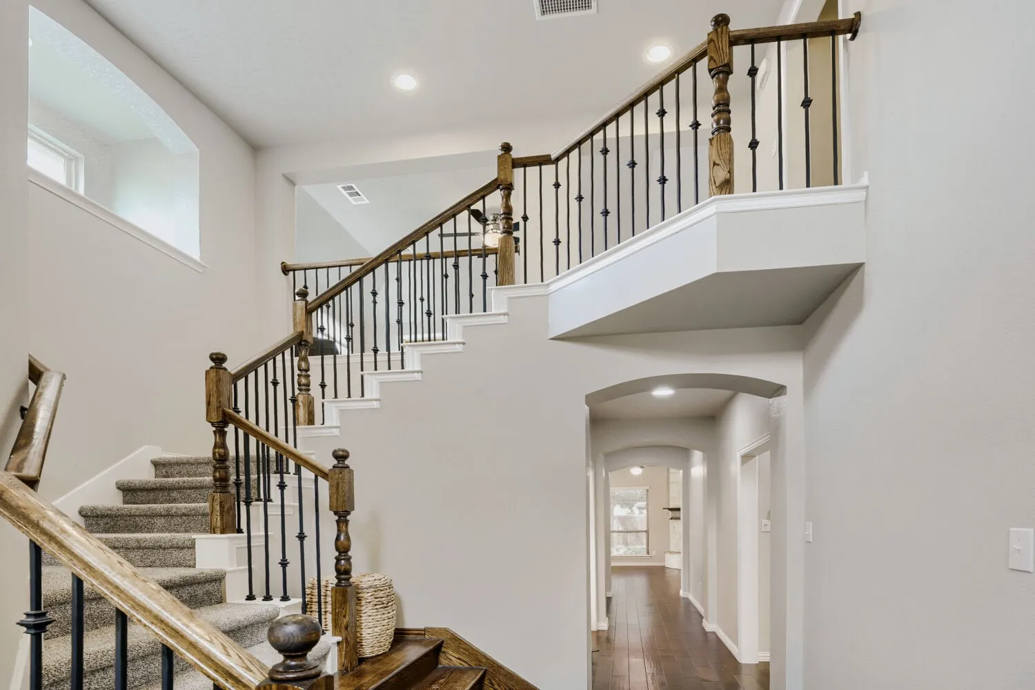 Grand staircase featuring wood railings with dark iron balusters and carpeted treads