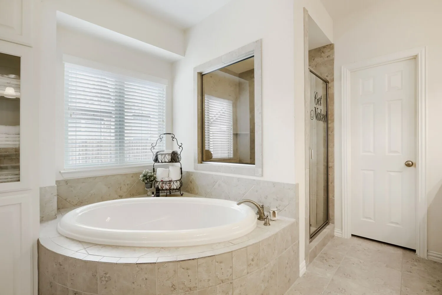 Soaking tub with a tiled surround, brushed nickel fixtures, and a large window with blinds
