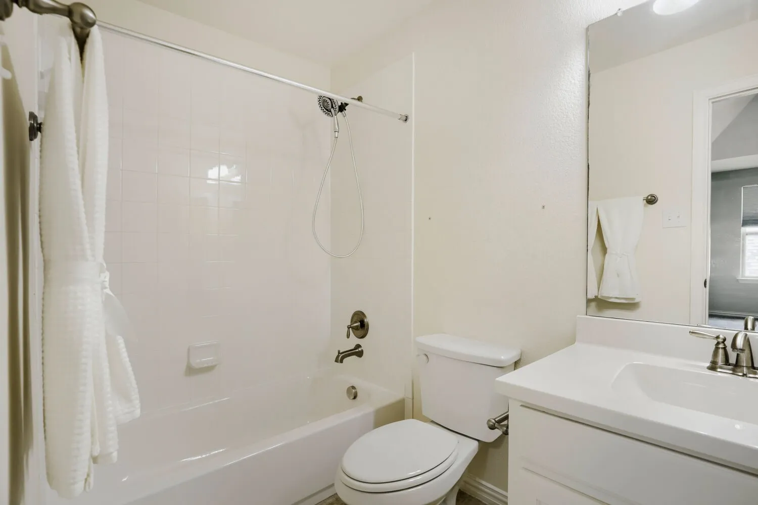 Full bathroom featuring a white porcelain tub and shower combination with a tiled surround, a white toilet, and a vanity with a white countertop and integrated sink