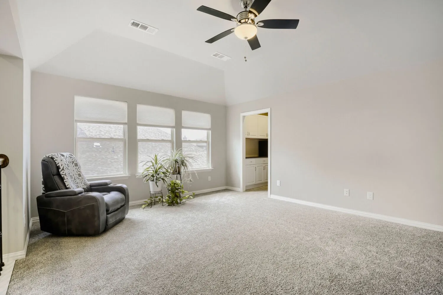 Carpeted room featuring a vaulted ceiling with a ceiling fan, three windows with blinds, and light gray wall paint
