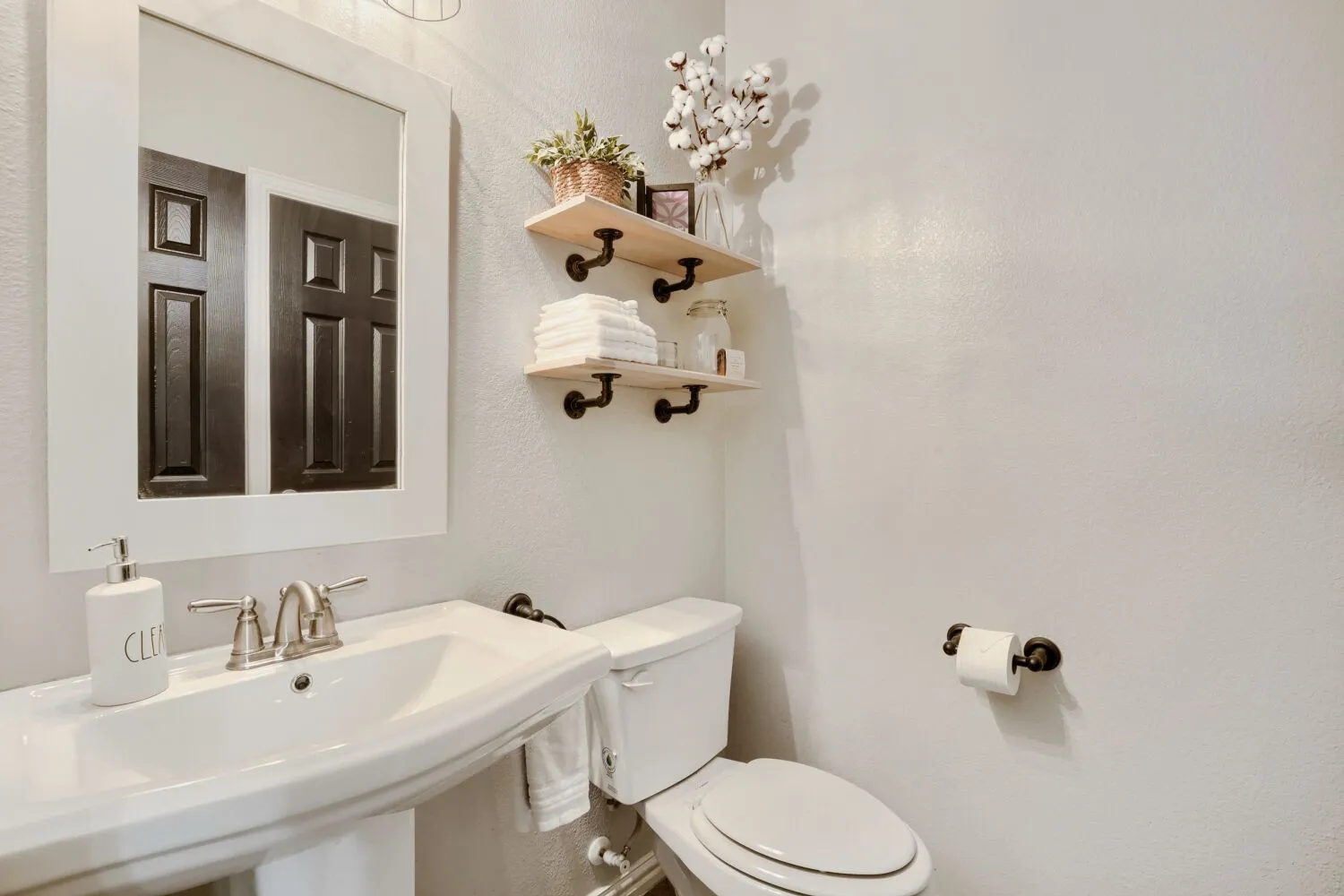 Pedestal sink with a brushed nickel faucet and a framed mirror