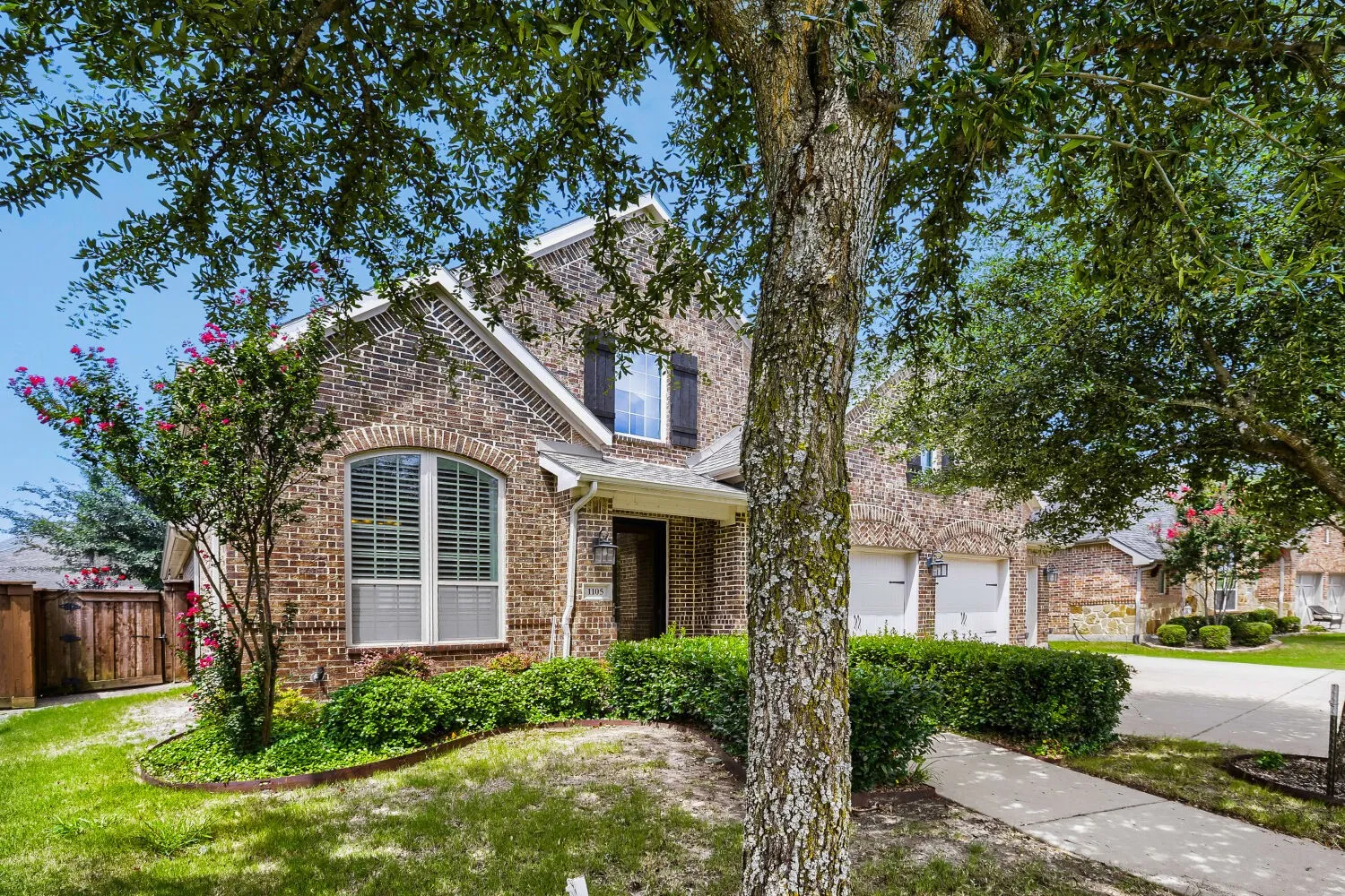 Traditional brick exterior featuring an arched window, dark shutters, a covered entry, and an attached two-car garage