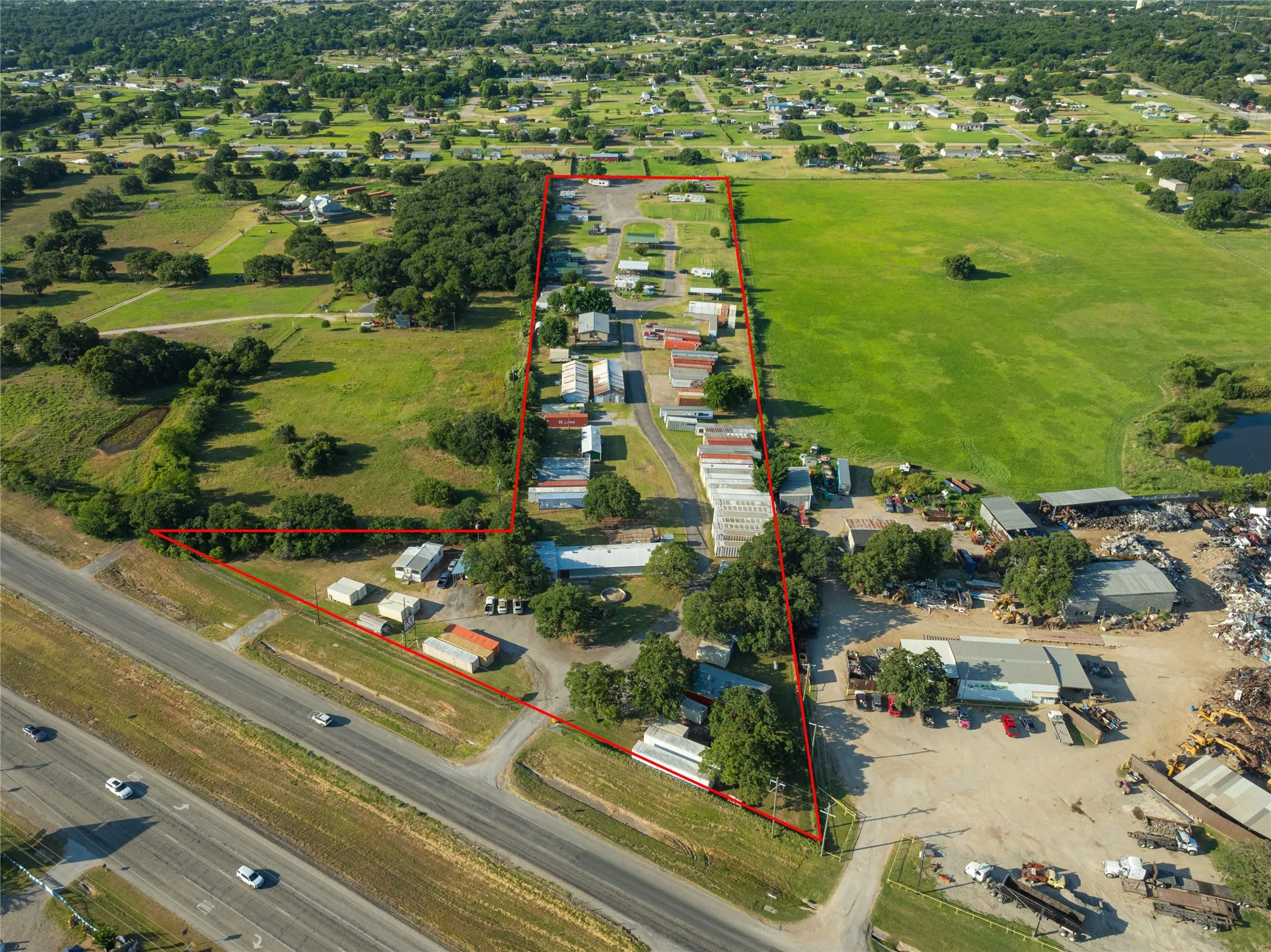 Expansive land parcel featuring direct highway frontage, extensive grassy areas, mature trees, and multiple existing structures
