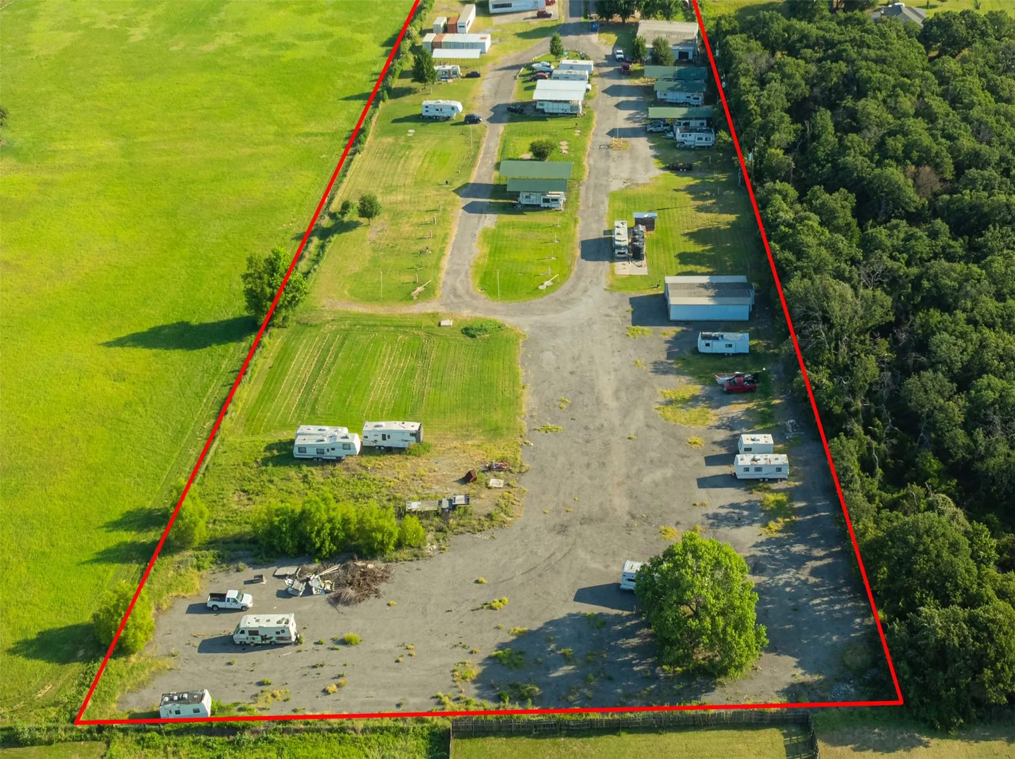 Expansive aerial view showcasing a large parcel of land outlined in red, featuring multiple recreational vehicle parking areas and several outbuildings