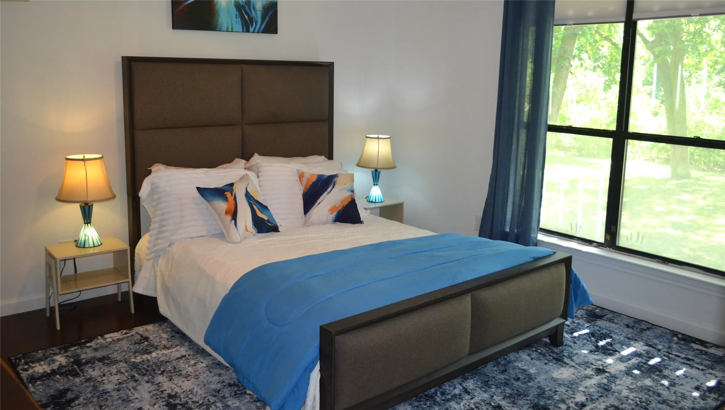 Bedroom featuring rich wood-finish flooring, a large window with exterior views, and white walls