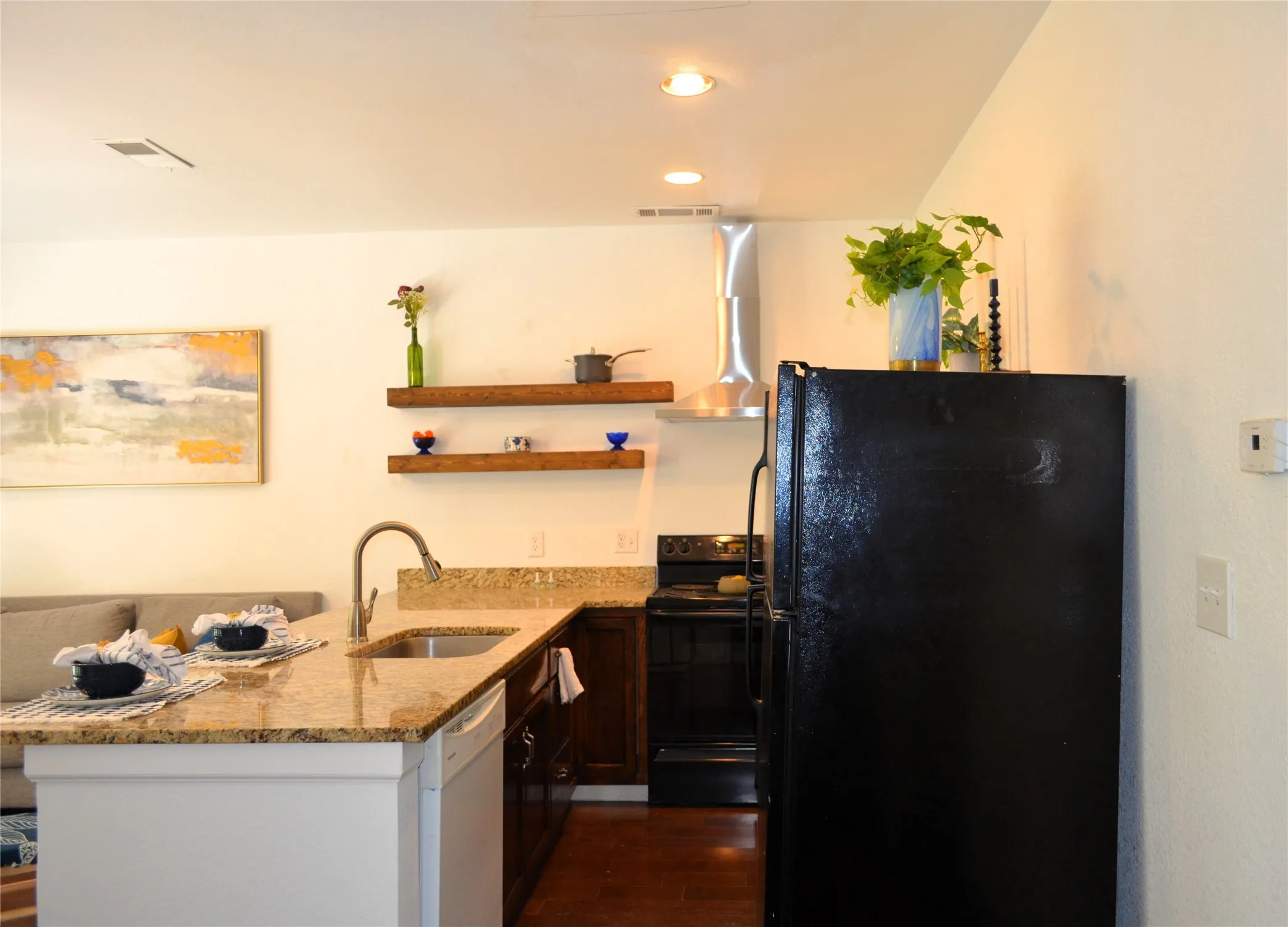 Contemporary kitchen featuring a stainless steel sink, granite countertops, white dishwasher, dark wood-finish cabinetry, and recessed lighting