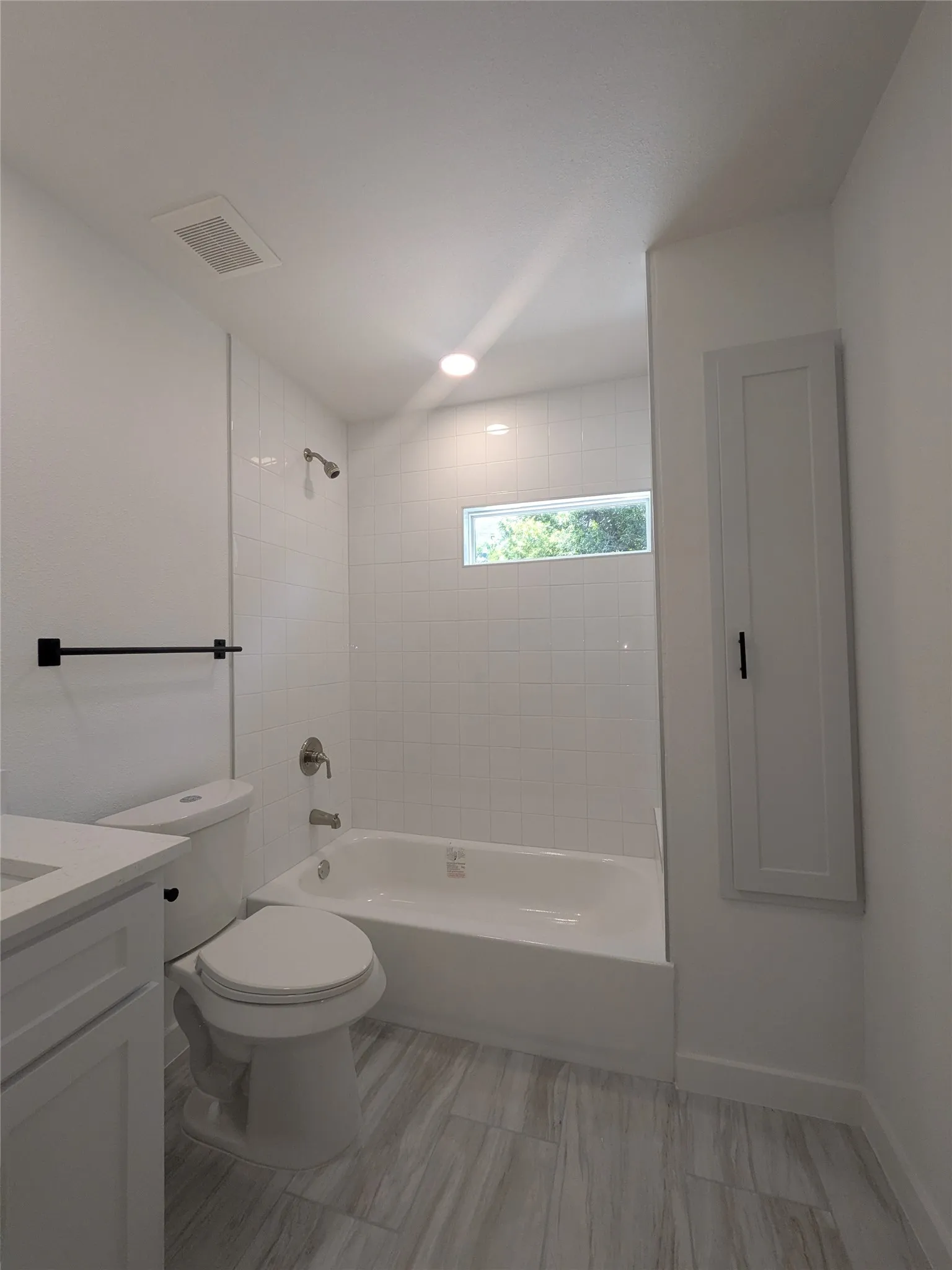 Full bathroom featuring a white tub/shower combination with subway tile surround, sleek gray wood-finish flooring, and a contemporary white vanity with a light countertop