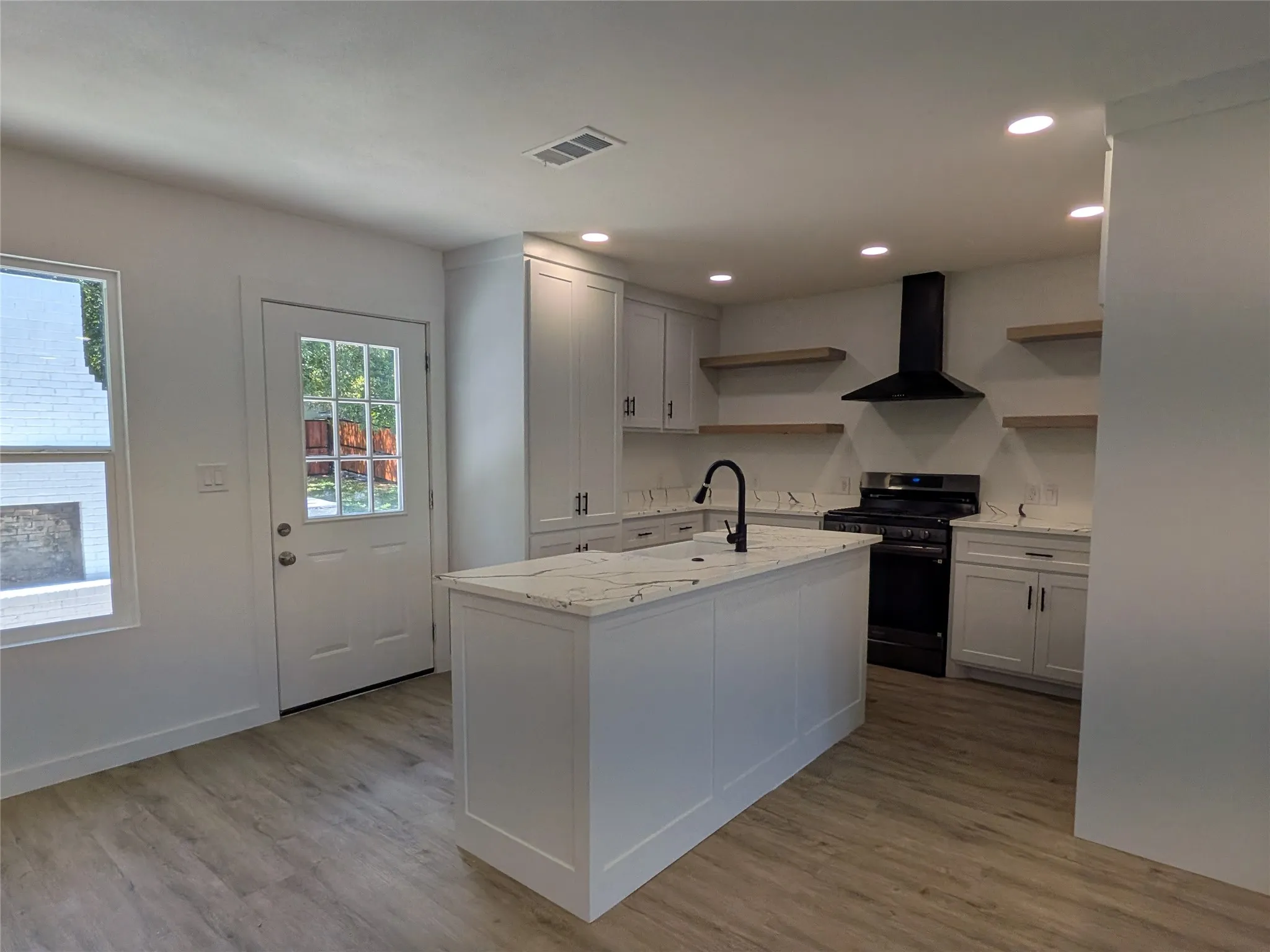 Modern kitchen featuring a central island with a solid surface countertop, white cabinetry, wood-finish flooring, a black range hood, and recessed lighting