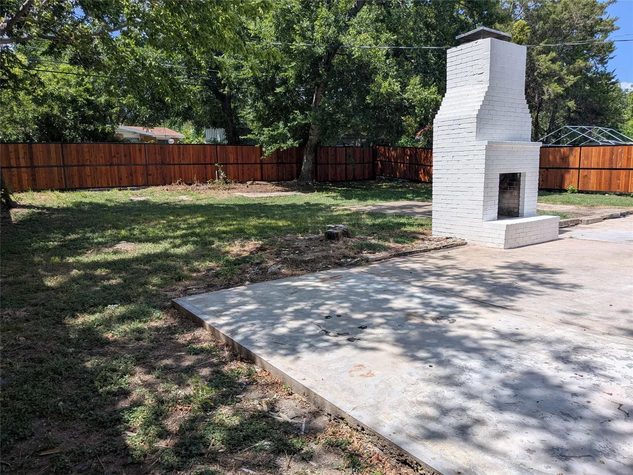 Expansive backyard featuring a white brick outdoor fireplace, a concrete patio, and a newly stained wood privacy fence
