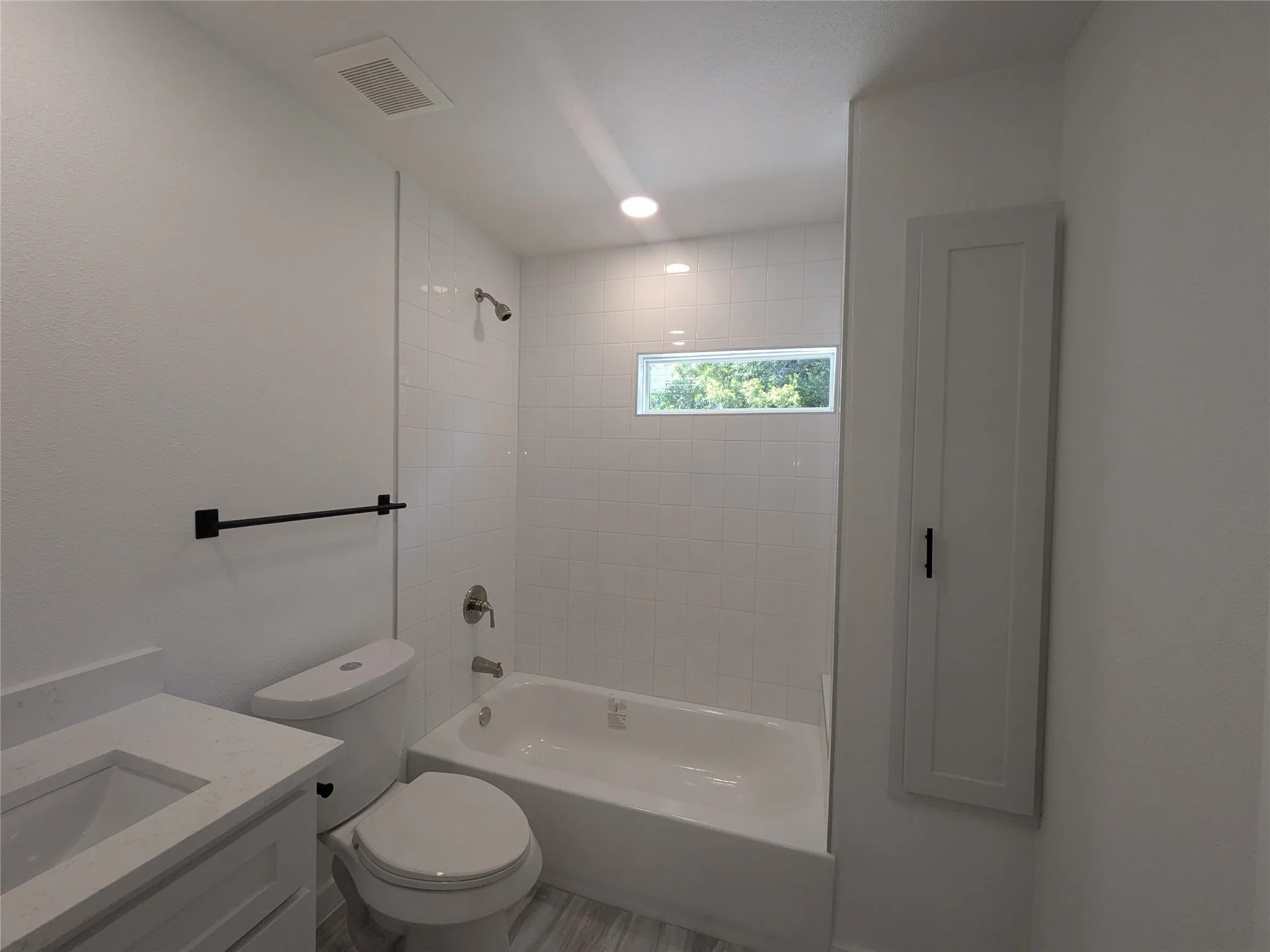 Bathroom featuring a white subway tile tub surround, white bathtub, and wood-finish plank flooring