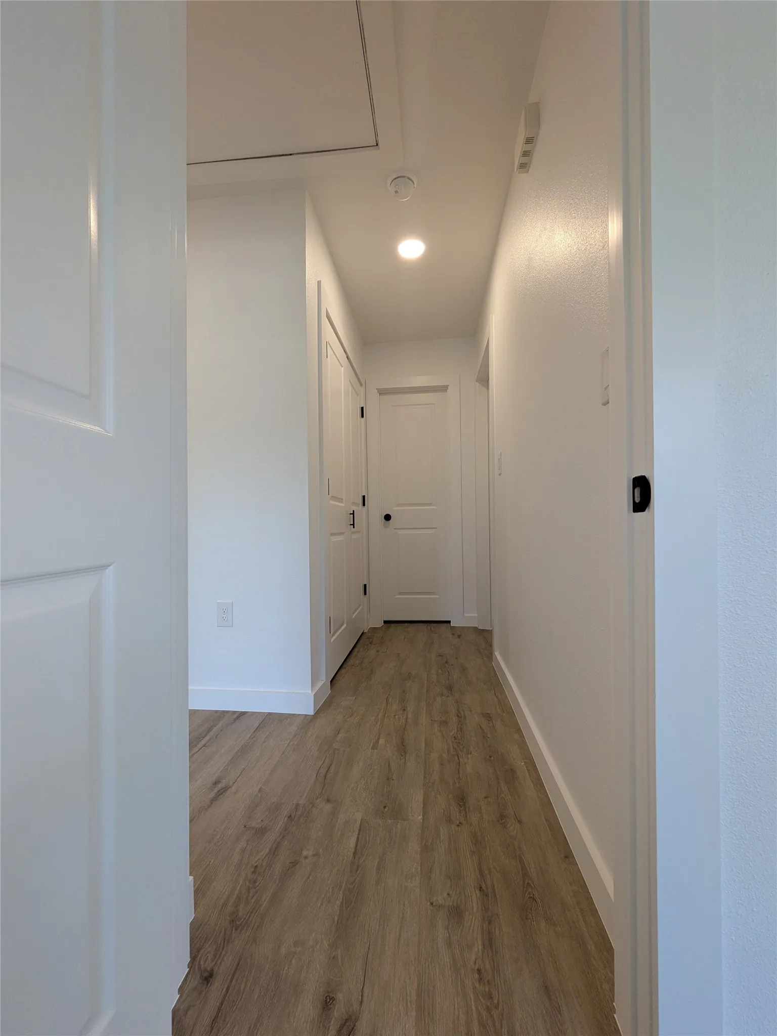 Hallway featuring wood-finish flooring, white paneled doors, recessed lighting, and crisp white baseboards